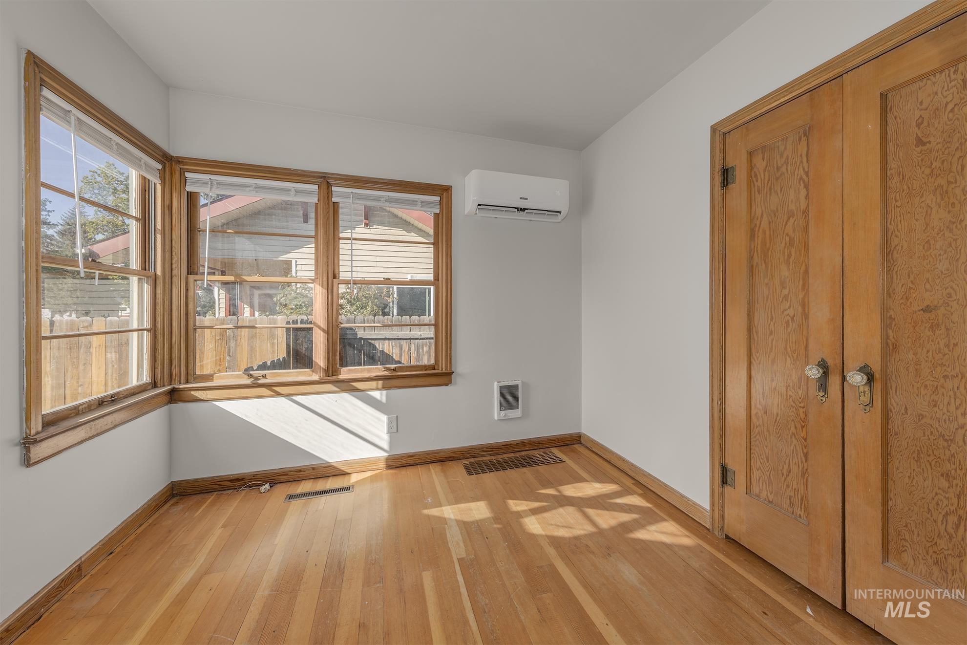 Unfurnished bedroom with light wood-style floors, an AC wall unit, and heating unit