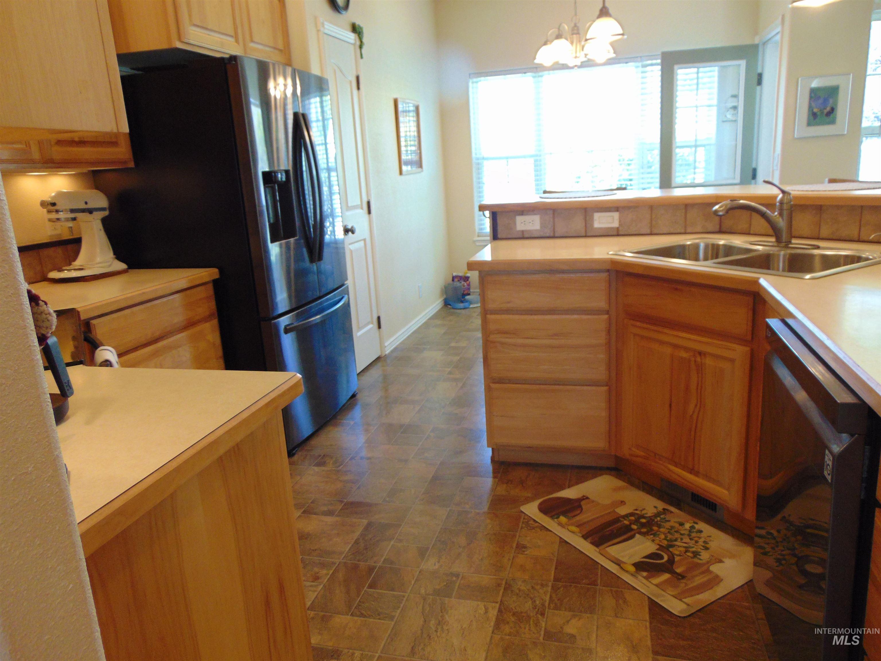 Kitchen with hanging light fixtures, light countertops, appliances with stainless steel finishes, a chandelier, and stone finish floors