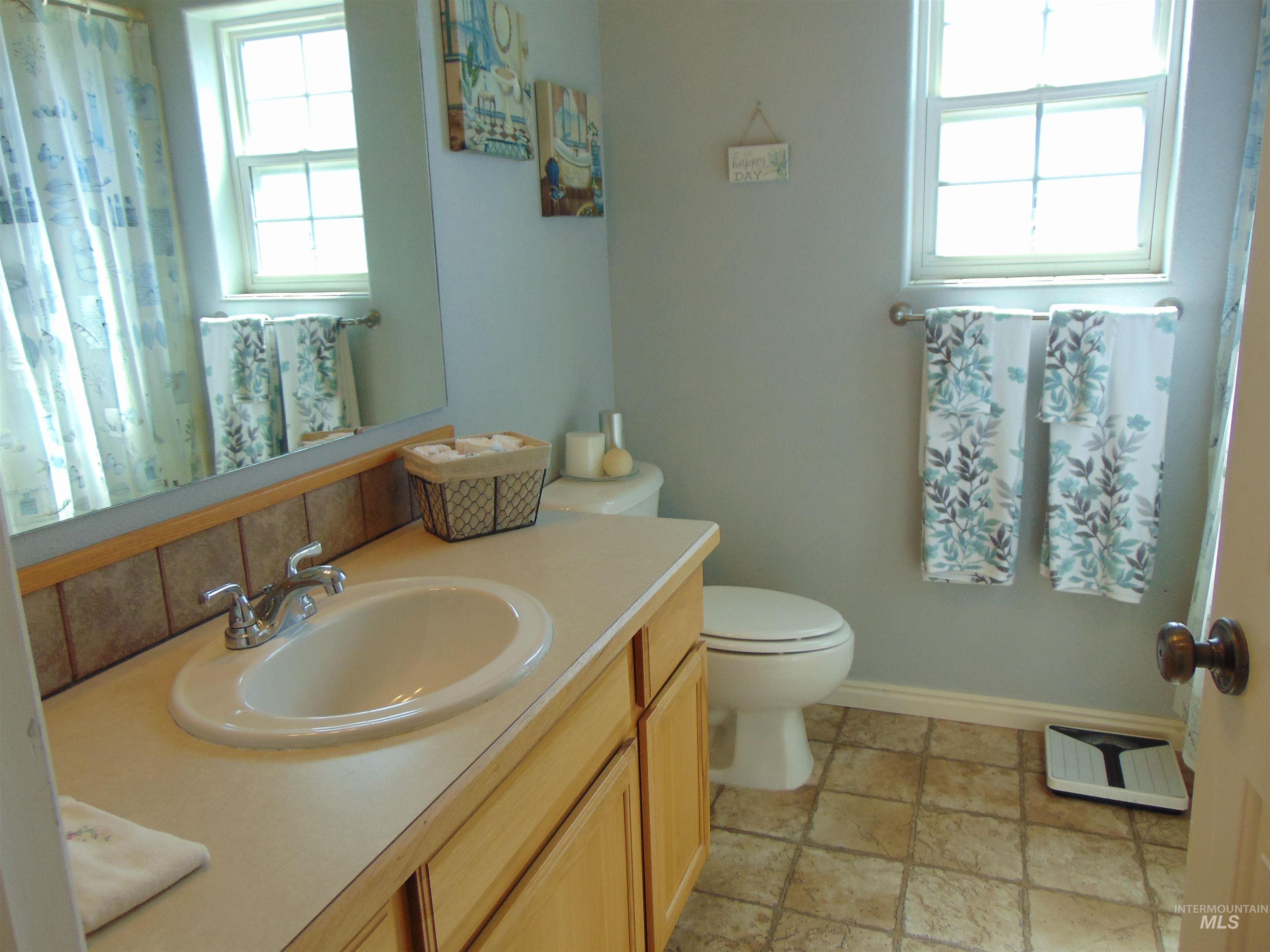 Full bath with healthy amount of natural light, vanity, light stone finish floors, and curtained shower