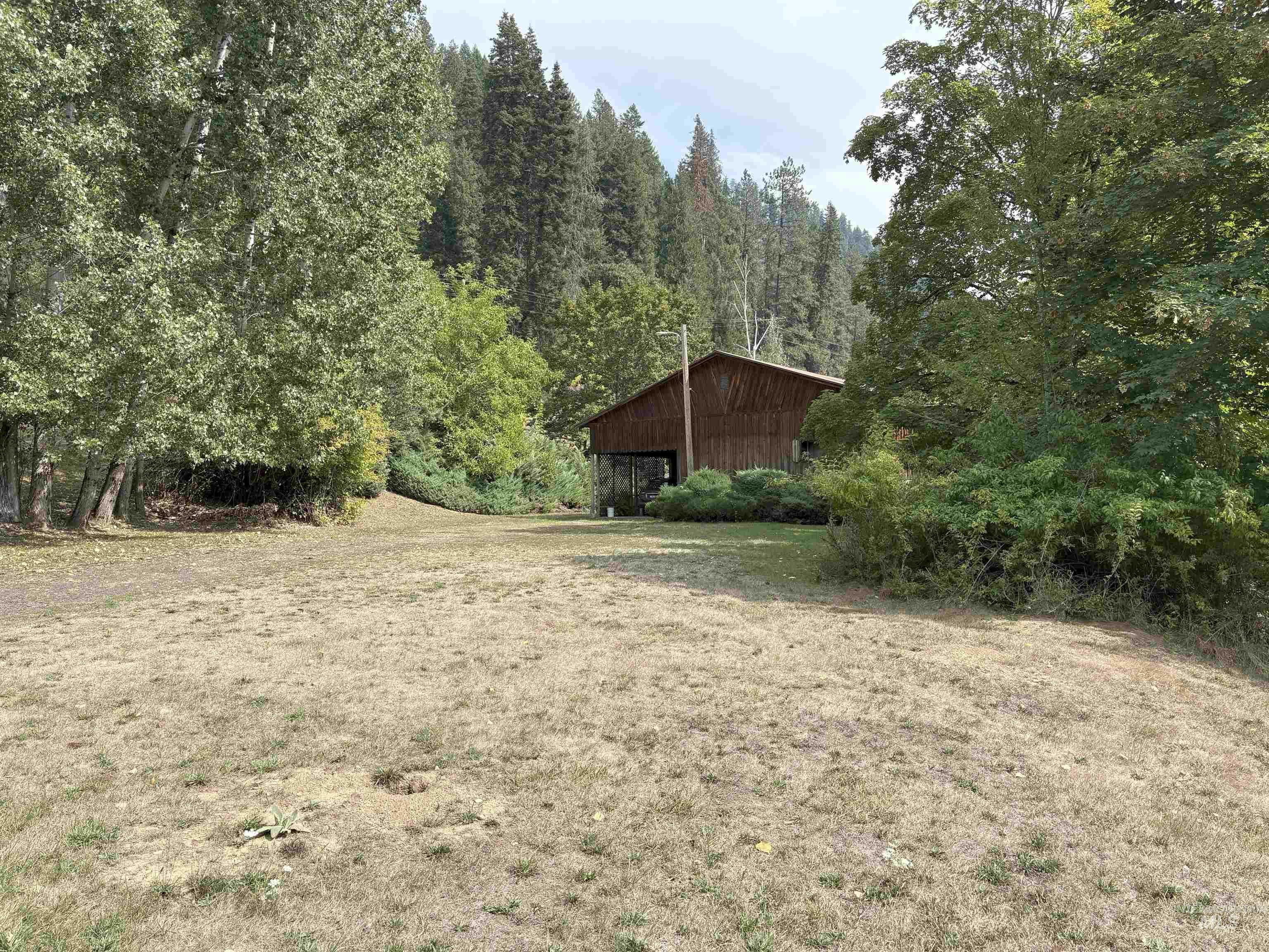 View of grassy yard featuring an outdoor structure, a wooded view, and a pole building