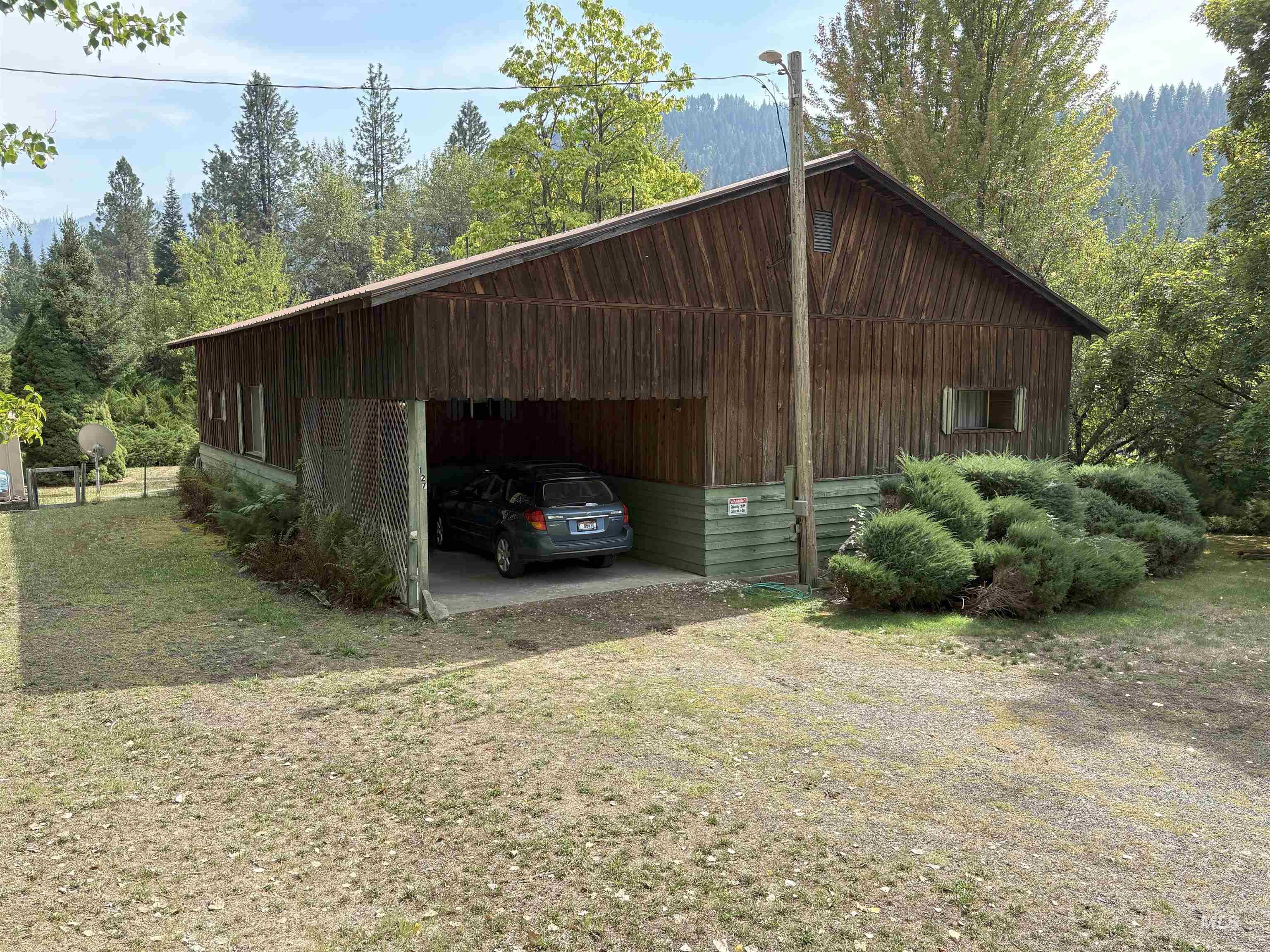 View of parking with a view of trees, a carport, and dirt driveway