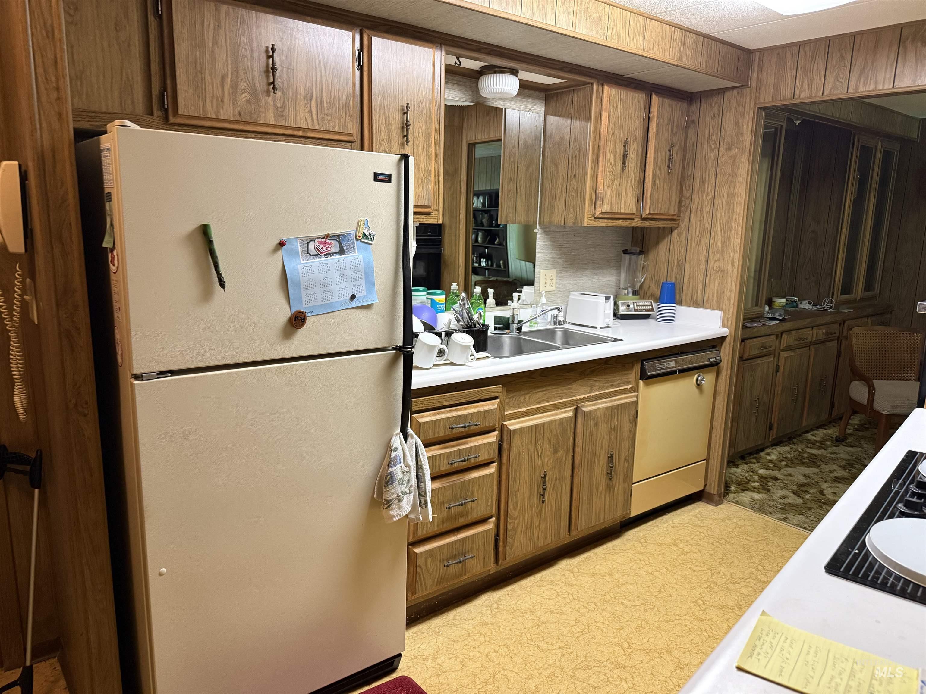 Kitchen featuring white appliances, light countertops, wood walls, and brown cabinetry