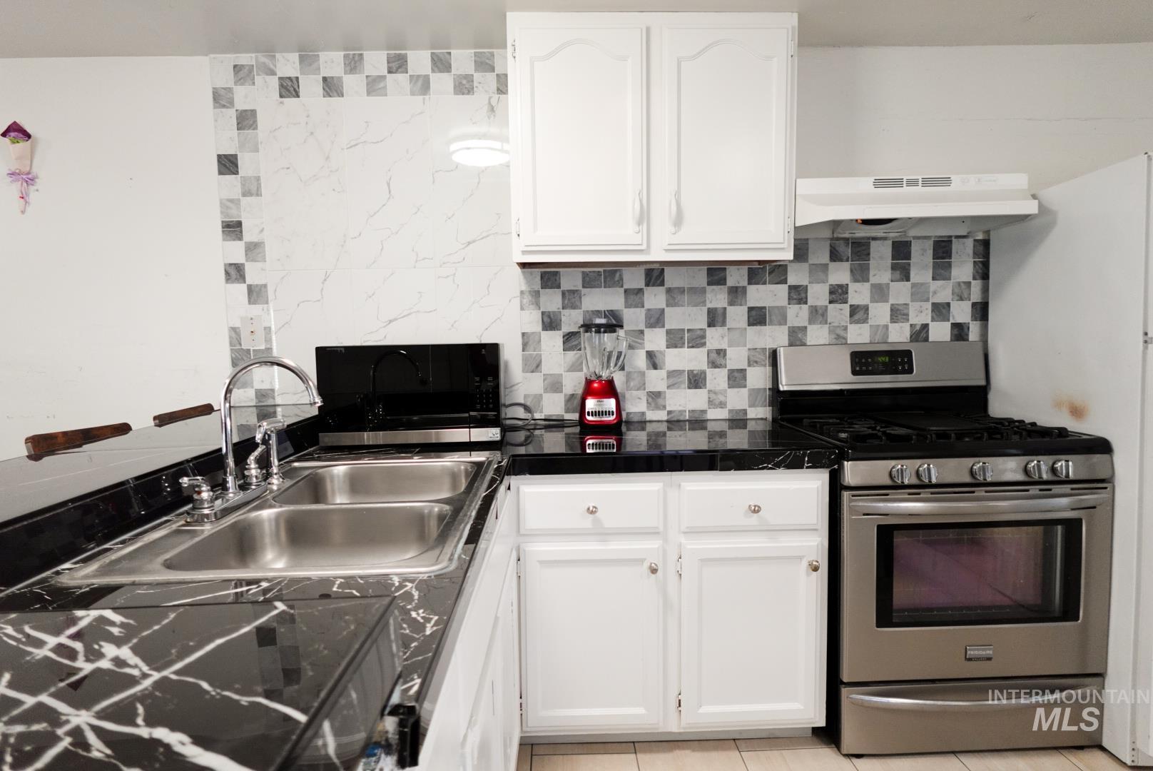 Kitchen with appliances with stainless steel finishes, white cabinetry, backsplash, under cabinet range hood, and dark countertops