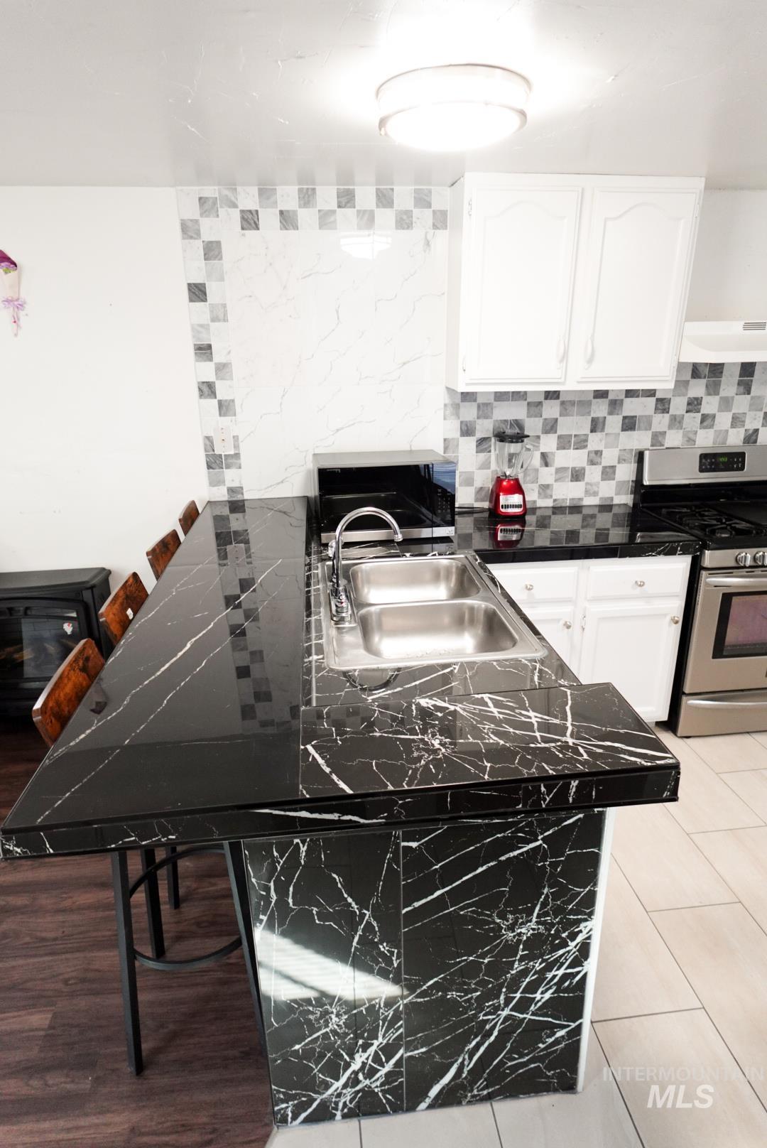 Kitchen featuring a kitchen bar, stainless steel appliances, decorative backsplash, white cabinetry, and under cabinet range hood