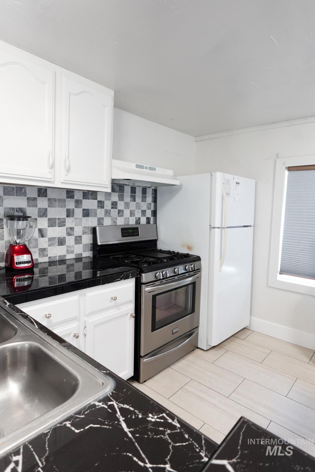 Kitchen featuring gas range, white cabinetry, backsplash, under cabinet range hood, and light wood-style flooring