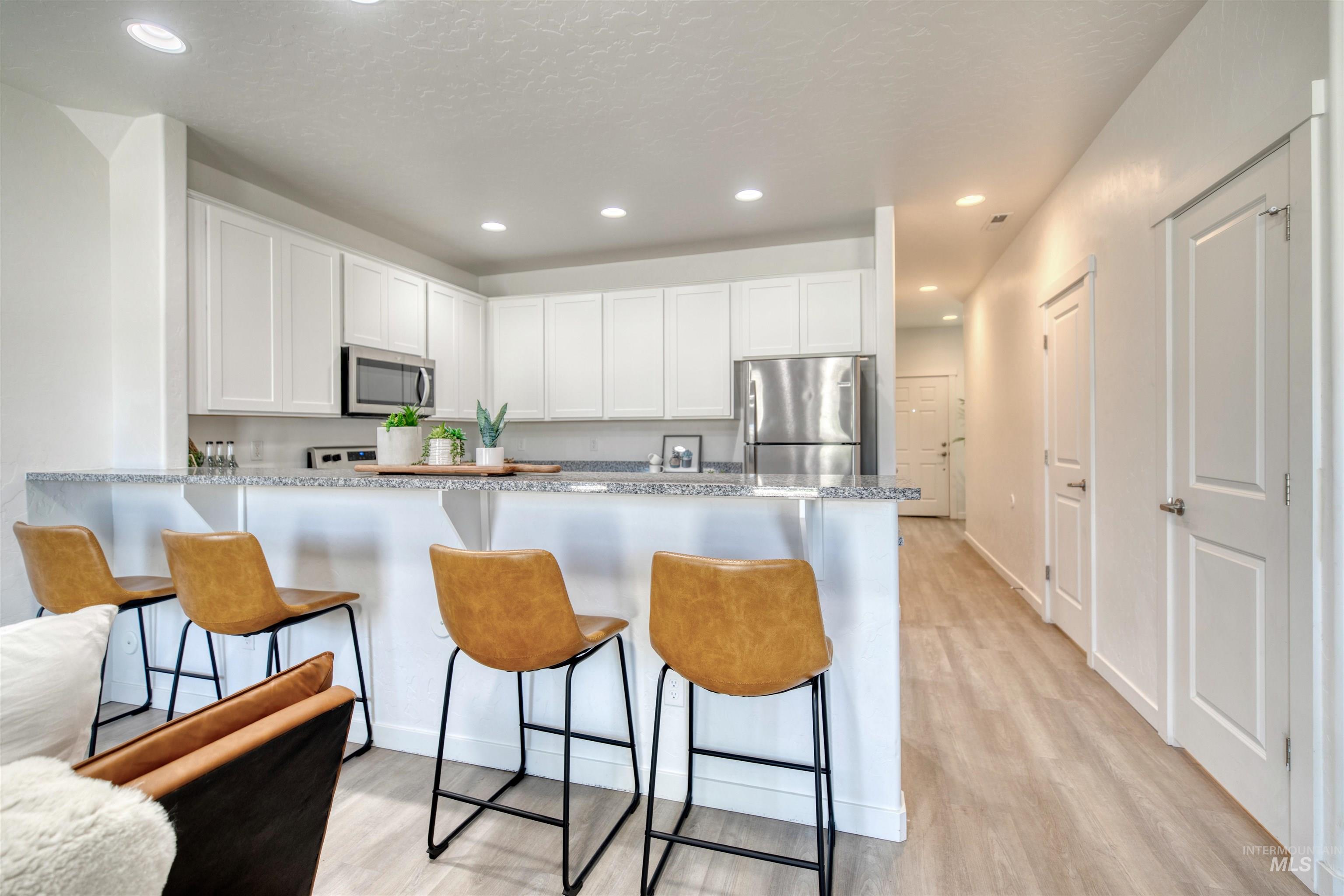 Kitchen with a breakfast bar, white cabinetry, a peninsula, recessed lighting, and light wood finished floors