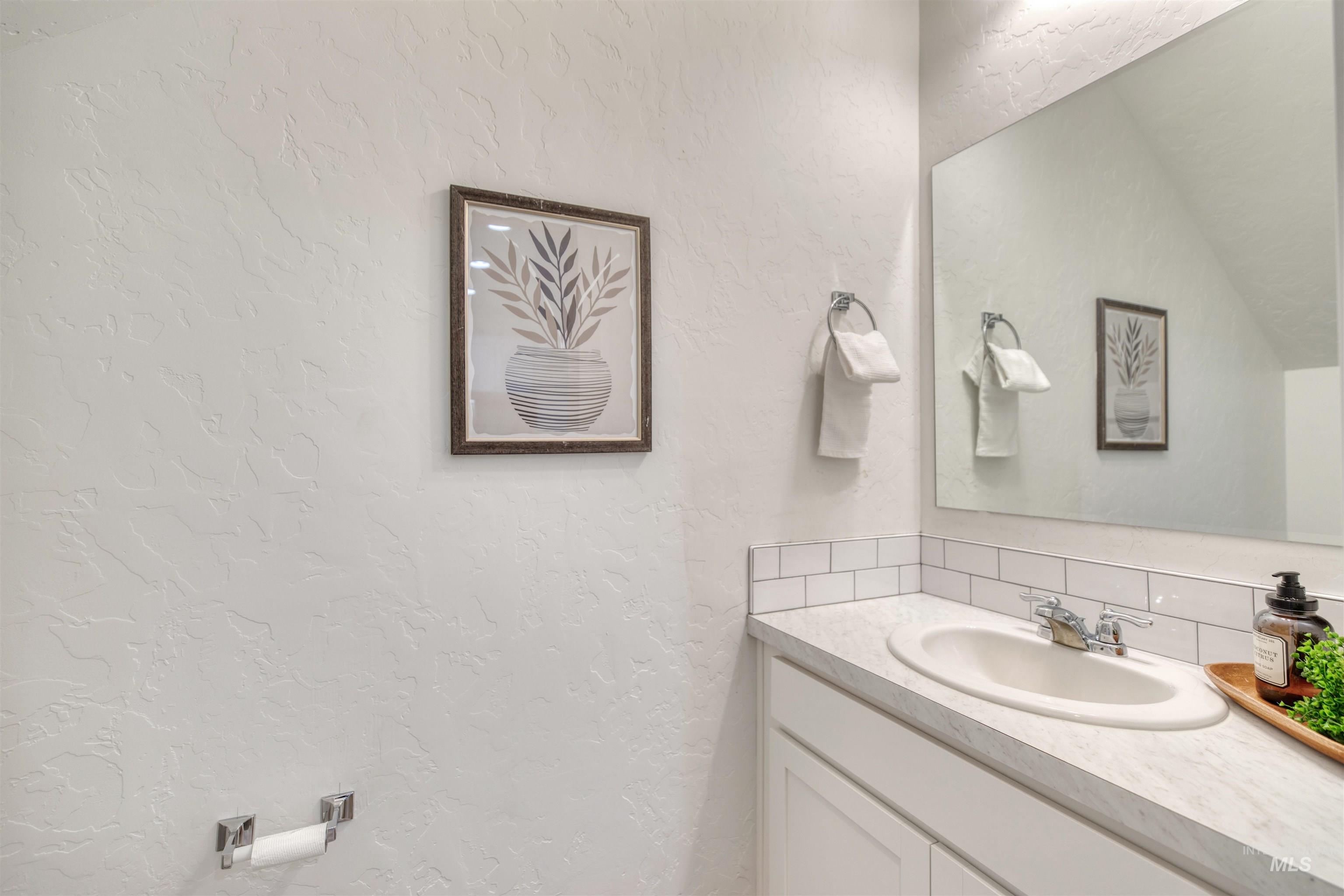 Bathroom with a textured wall, vanity, and tasteful backsplash
