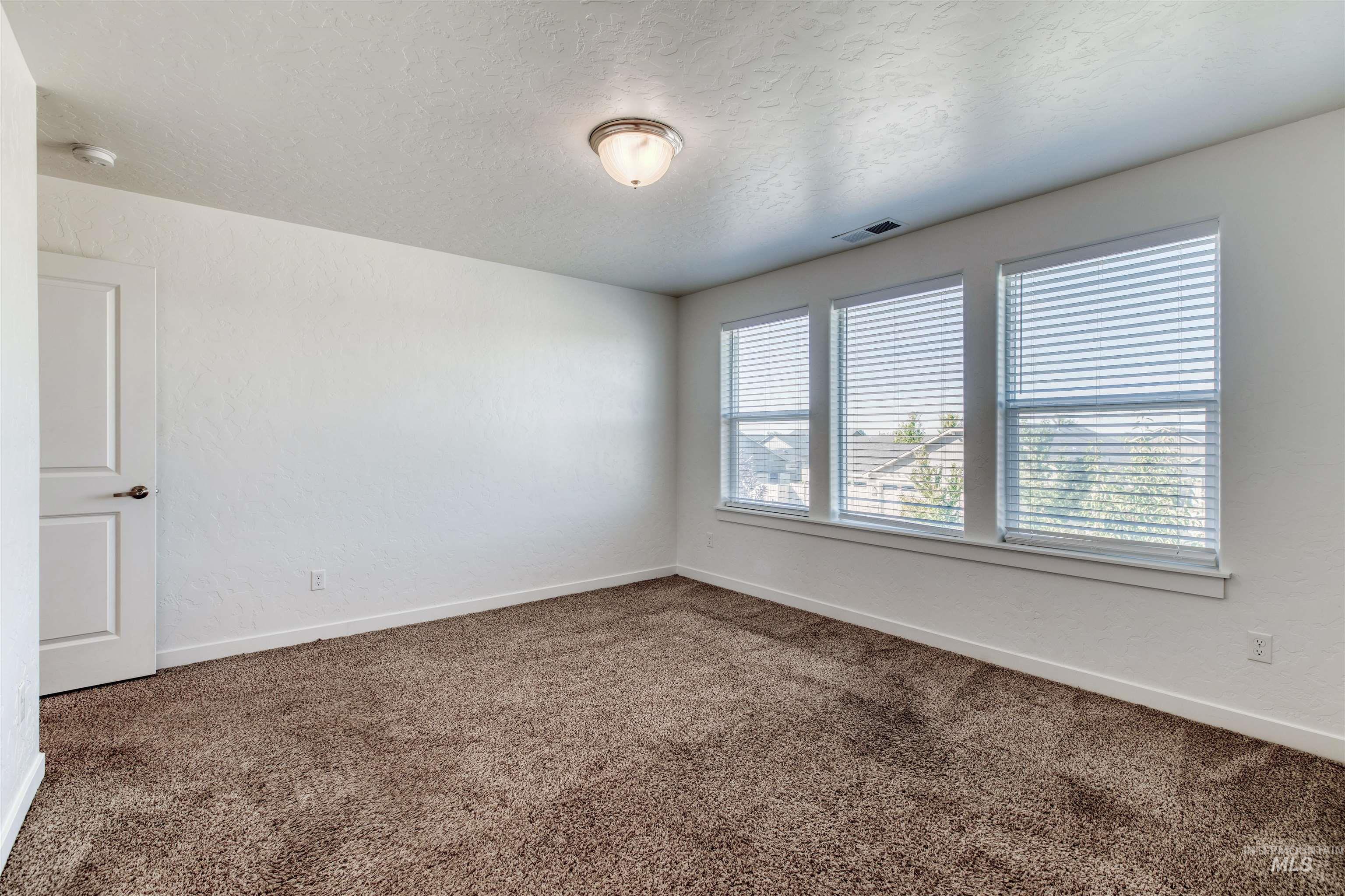 Carpeted spare room featuring a textured ceiling and baseboards