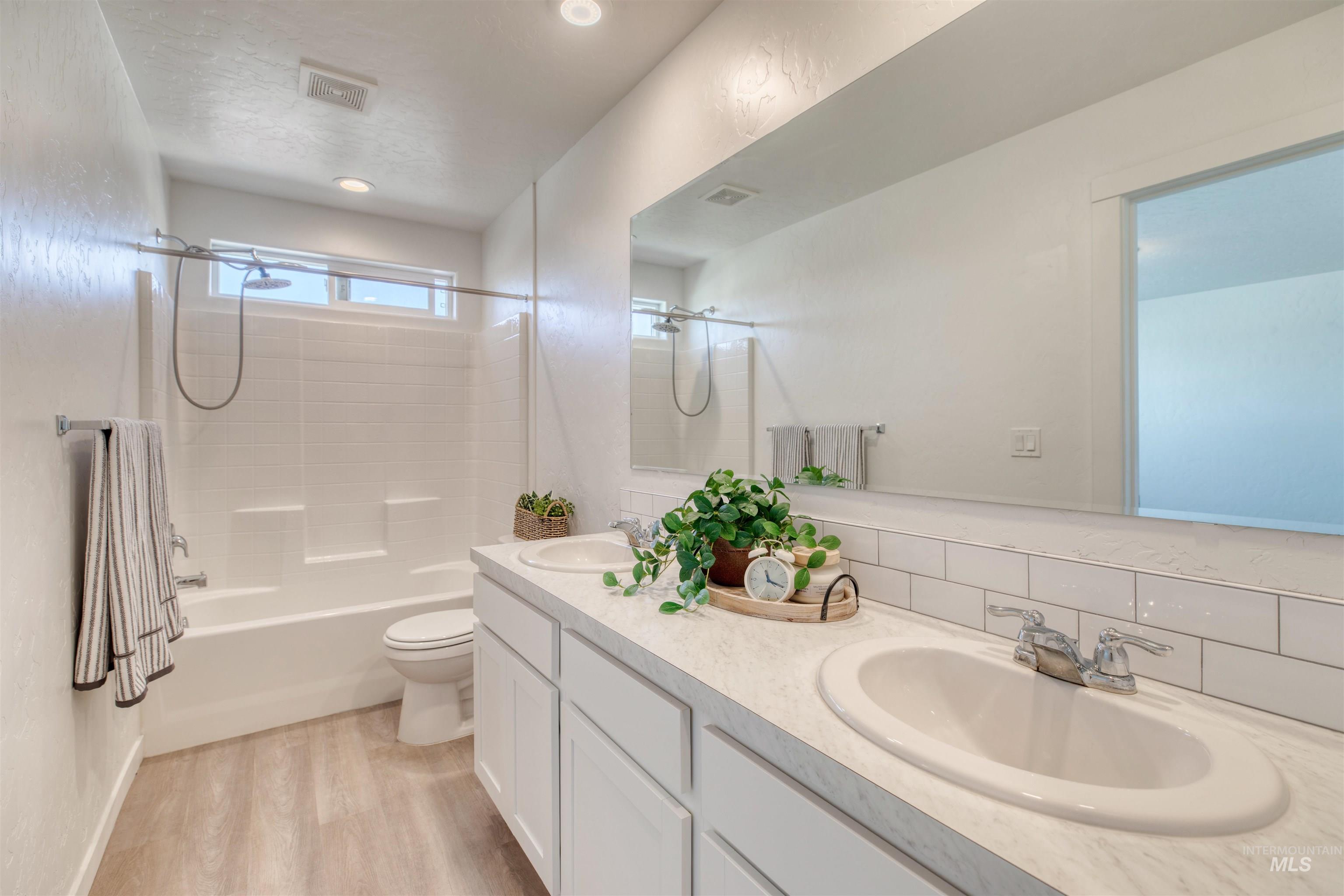 Full bath with washtub / shower combination, light wood-type flooring, double vanity, and decorative backsplash