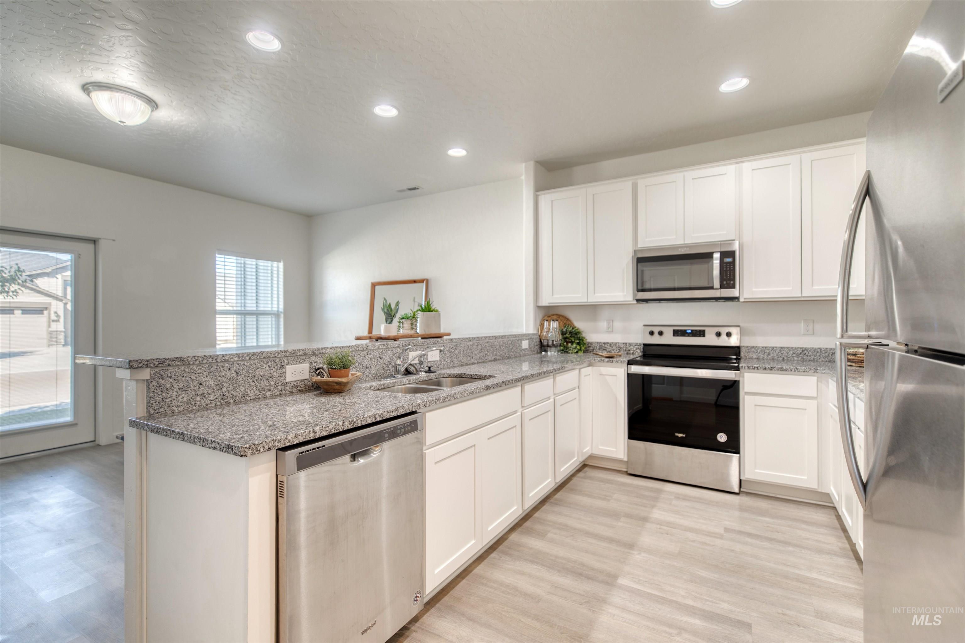 Kitchen featuring a peninsula, appliances with stainless steel finishes, white cabinetry, recessed lighting, and light stone countertops