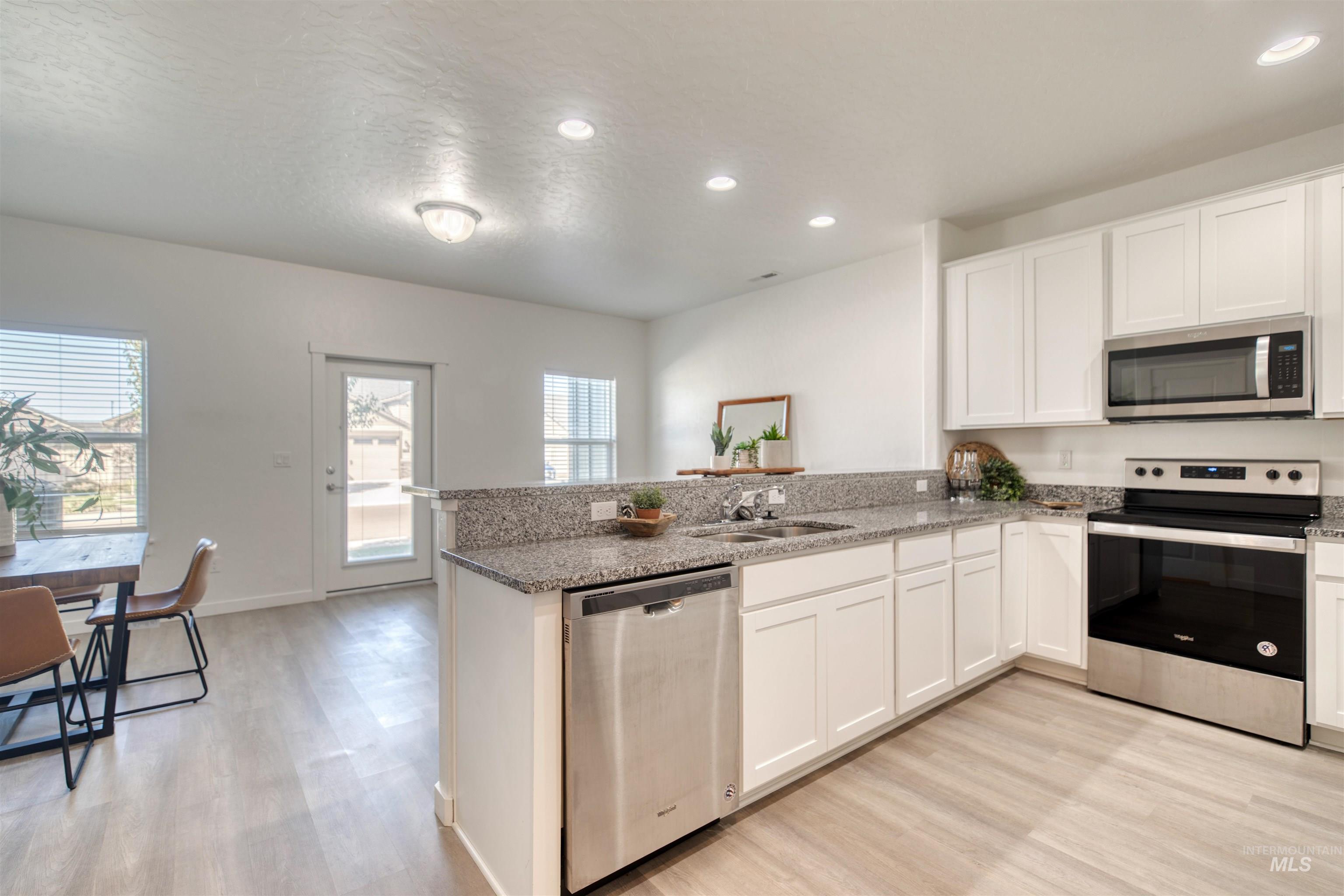 Kitchen with stainless steel appliances, a peninsula, white cabinetry, light stone counters, and recessed lighting