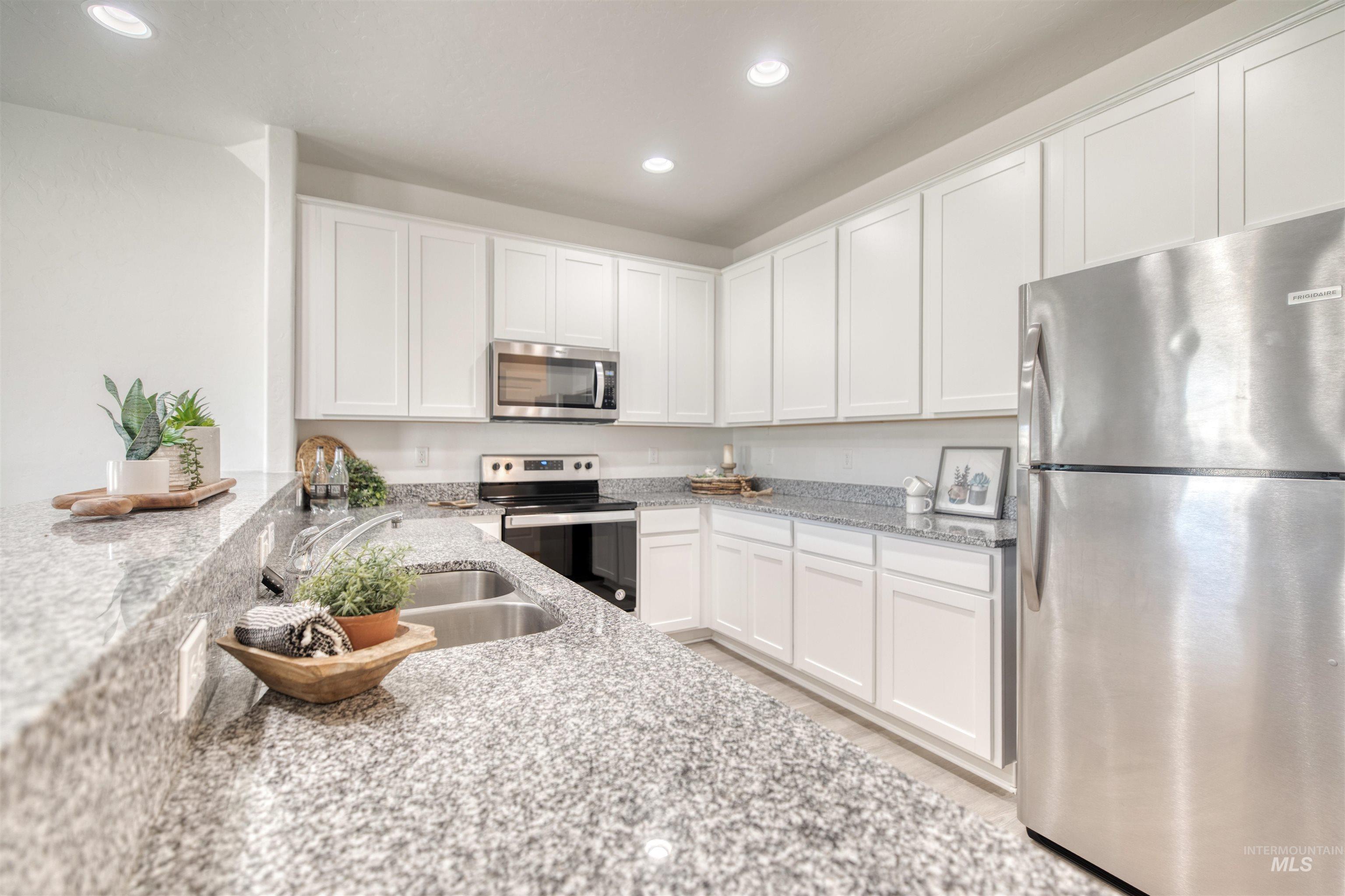 Kitchen with stainless steel appliances, white cabinetry, light stone counters, and recessed lighting