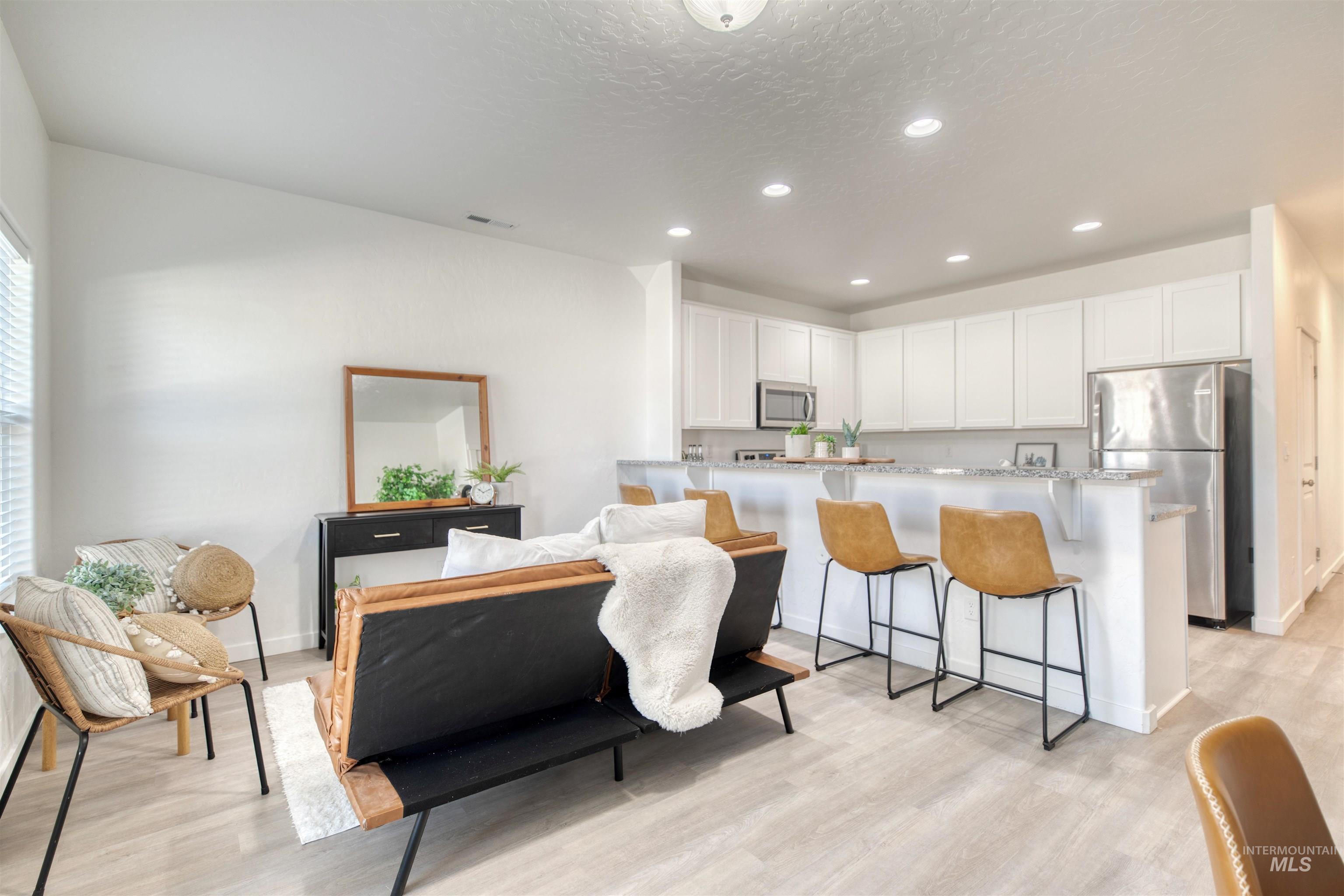 Kitchen with white cabinetry, a kitchen bar, appliances with stainless steel finishes, recessed lighting, and light wood finished floors