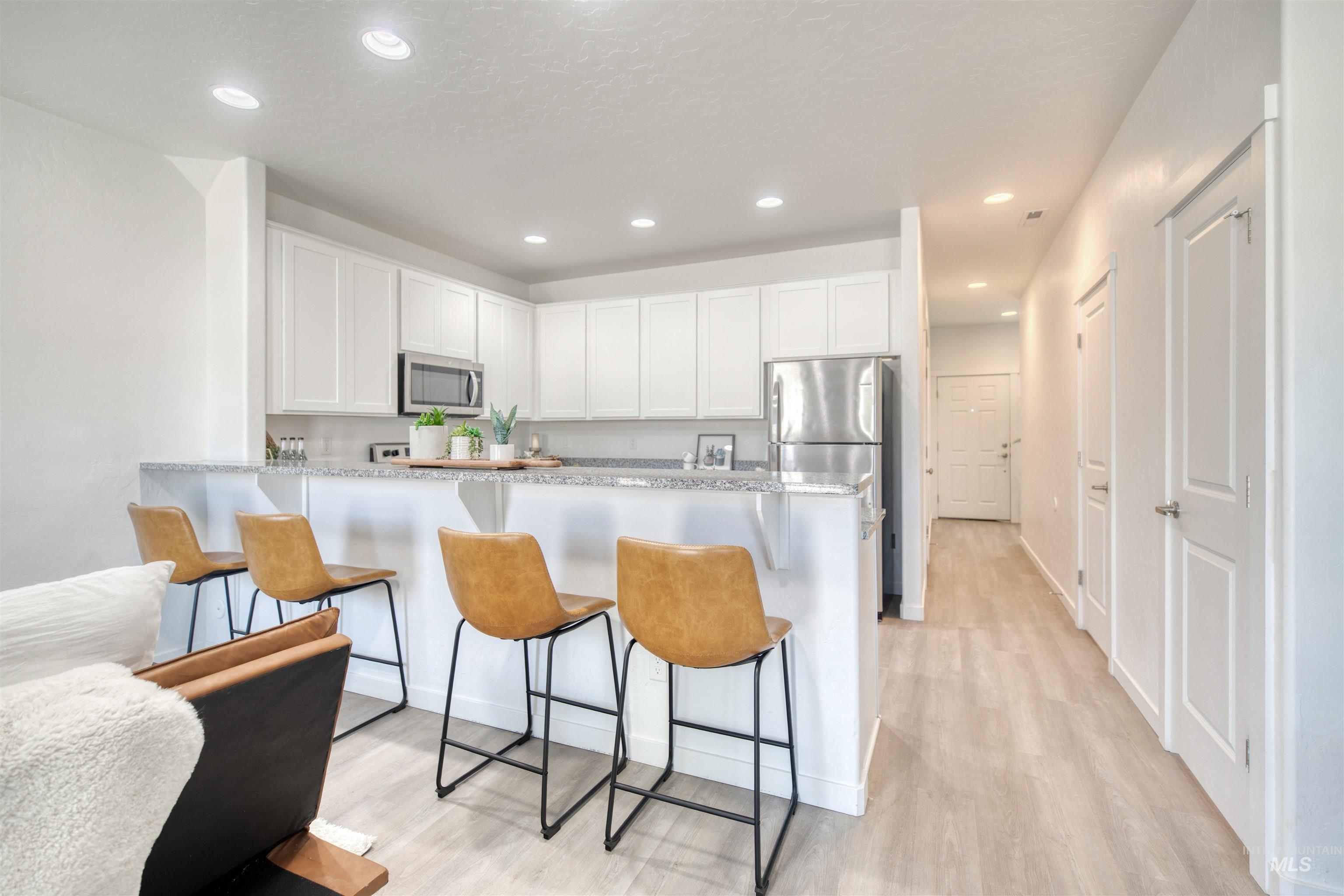 Kitchen with white cabinets, a breakfast bar area, a peninsula, recessed lighting, and appliances with stainless steel finishes
