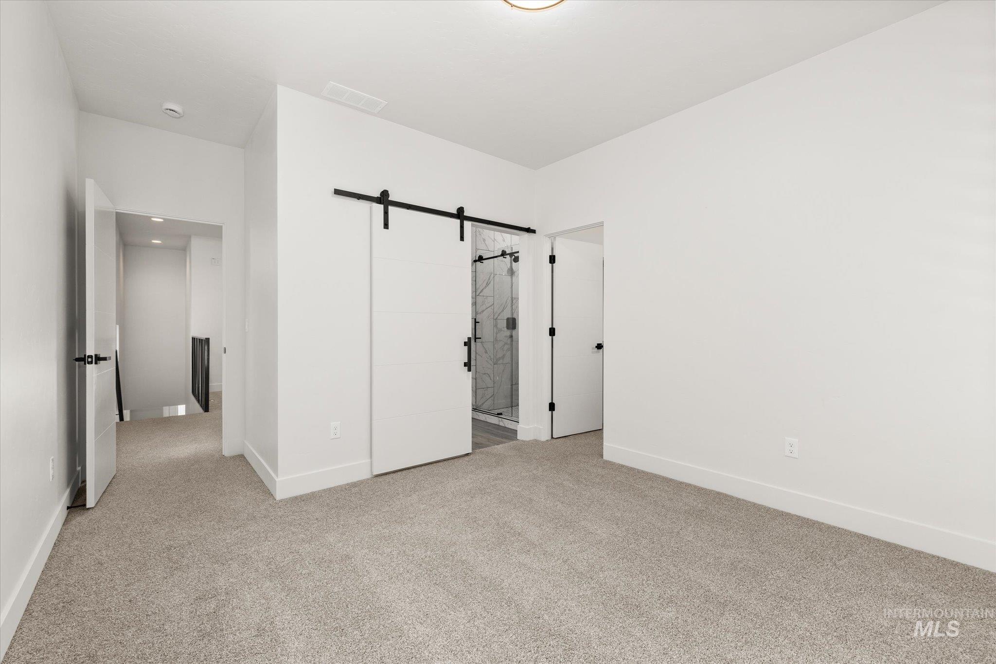 Unfurnished bedroom with a barn door, ensuite bath, and light carpet