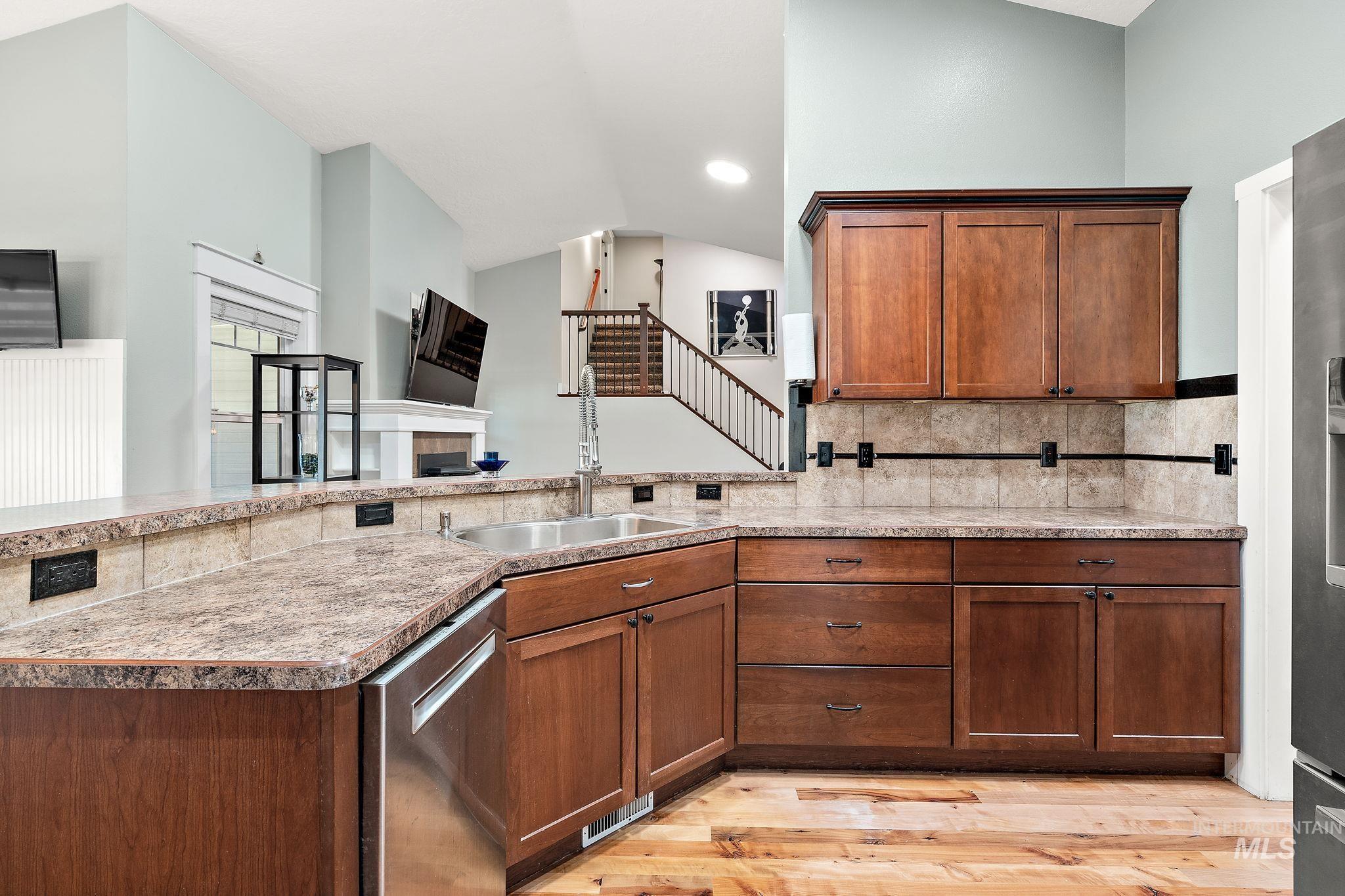 Kitchen with brown cabinets, stainless steel appliances, light wood-style flooring, a peninsula, and lofted ceiling
