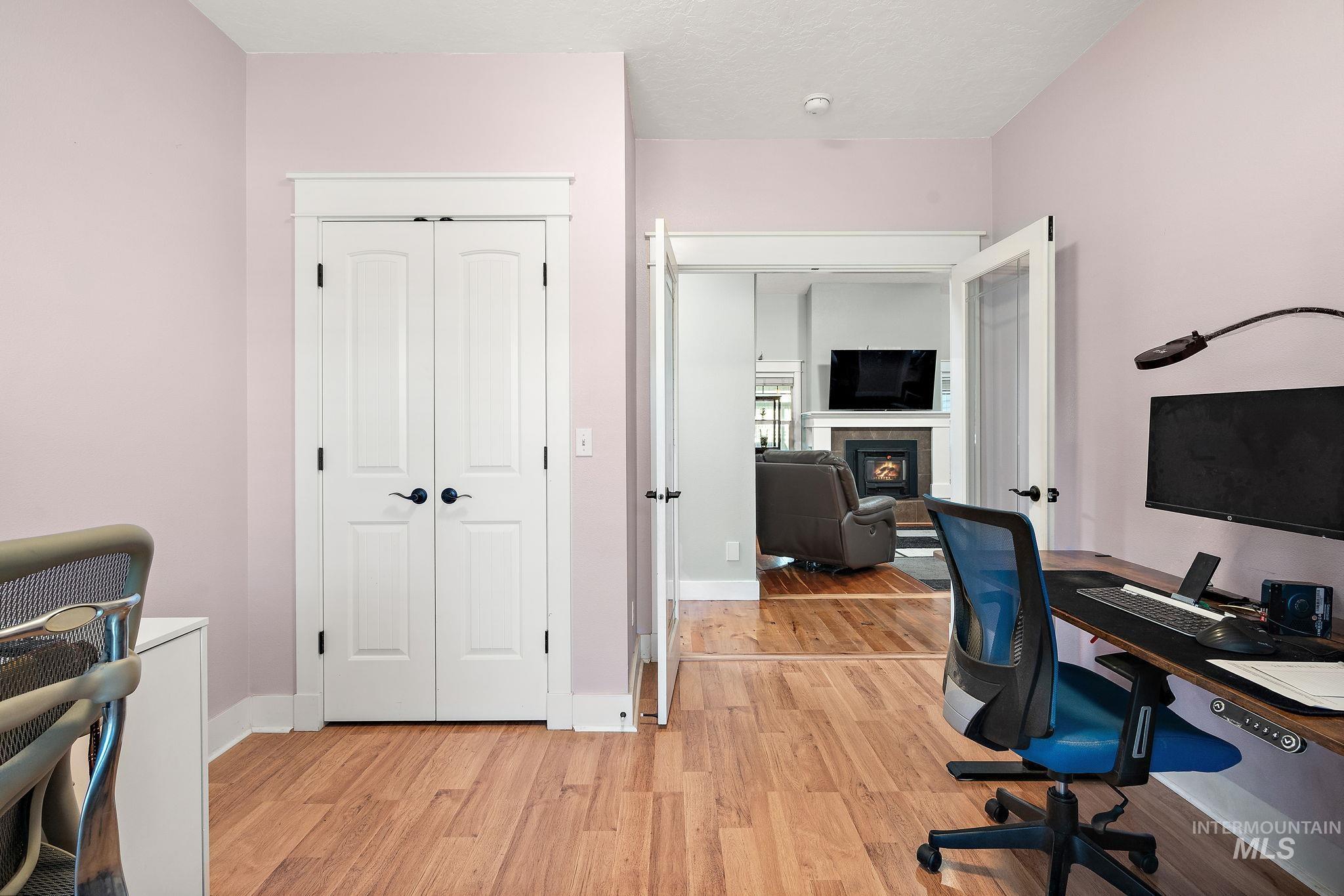 Home office with light wood finished floors and a warm lit fireplace