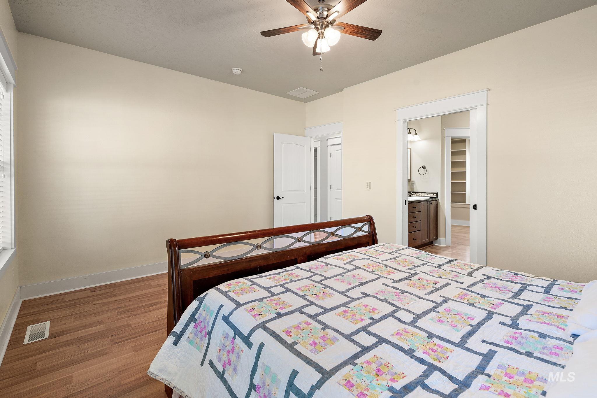 Bedroom with light wood-style flooring, a ceiling fan, and ensuite bath