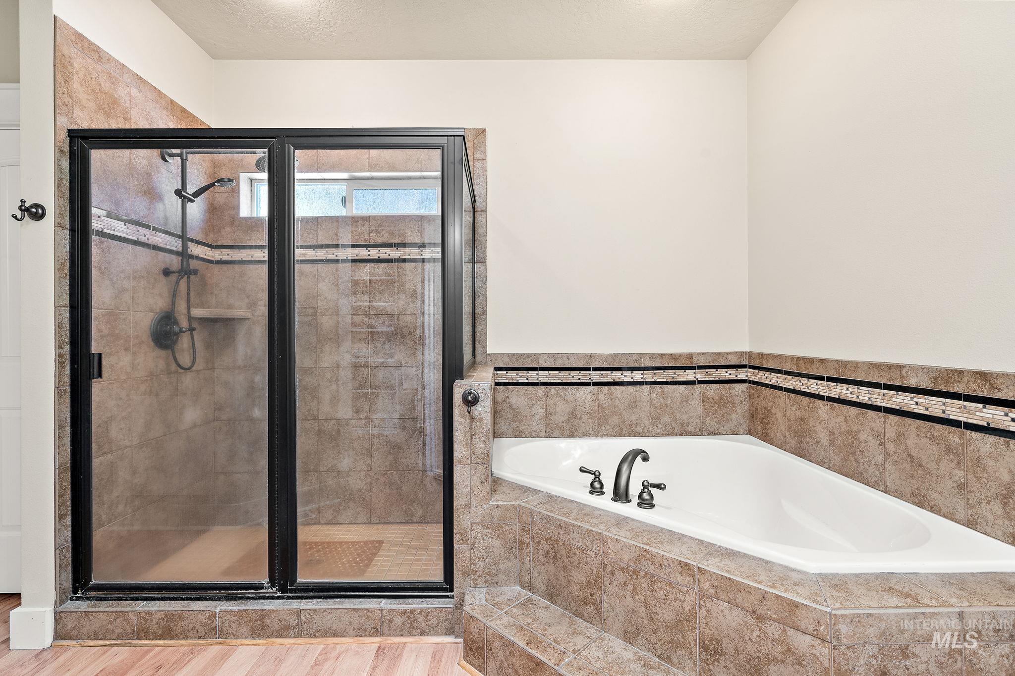 Bathroom with a garden tub, a shower stall, wood finished floors, and a textured ceiling