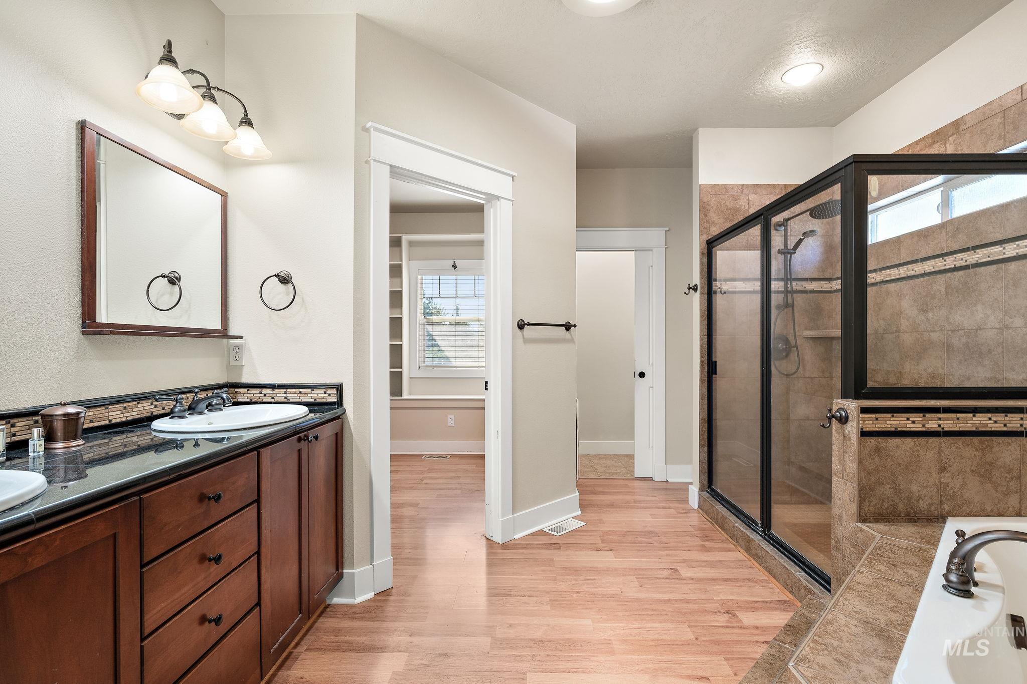 Full bath with double vanity, a shower stall, a bath, and light wood-type flooring