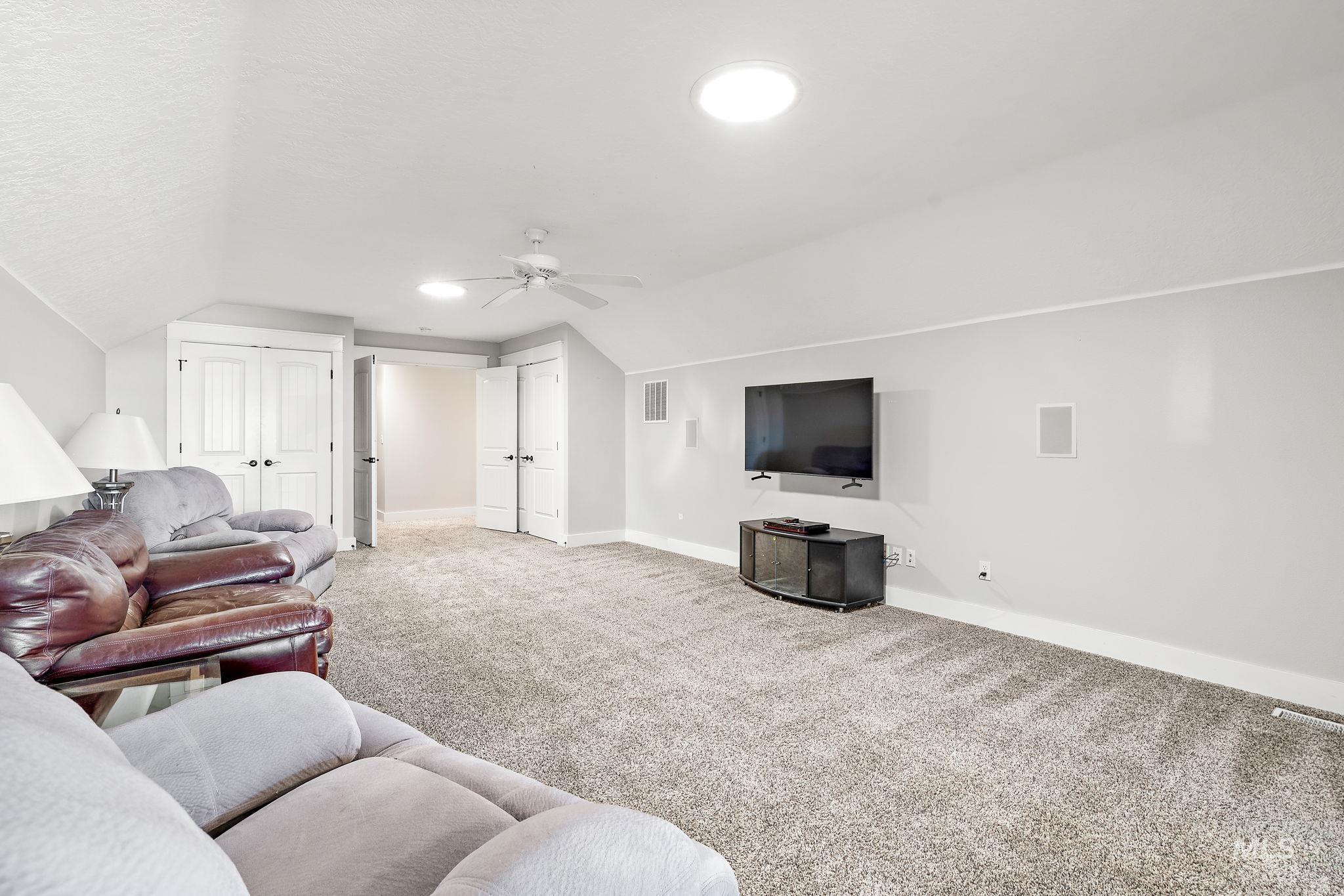 Carpeted living room with vaulted ceiling, a ceiling fan, and a textured ceiling