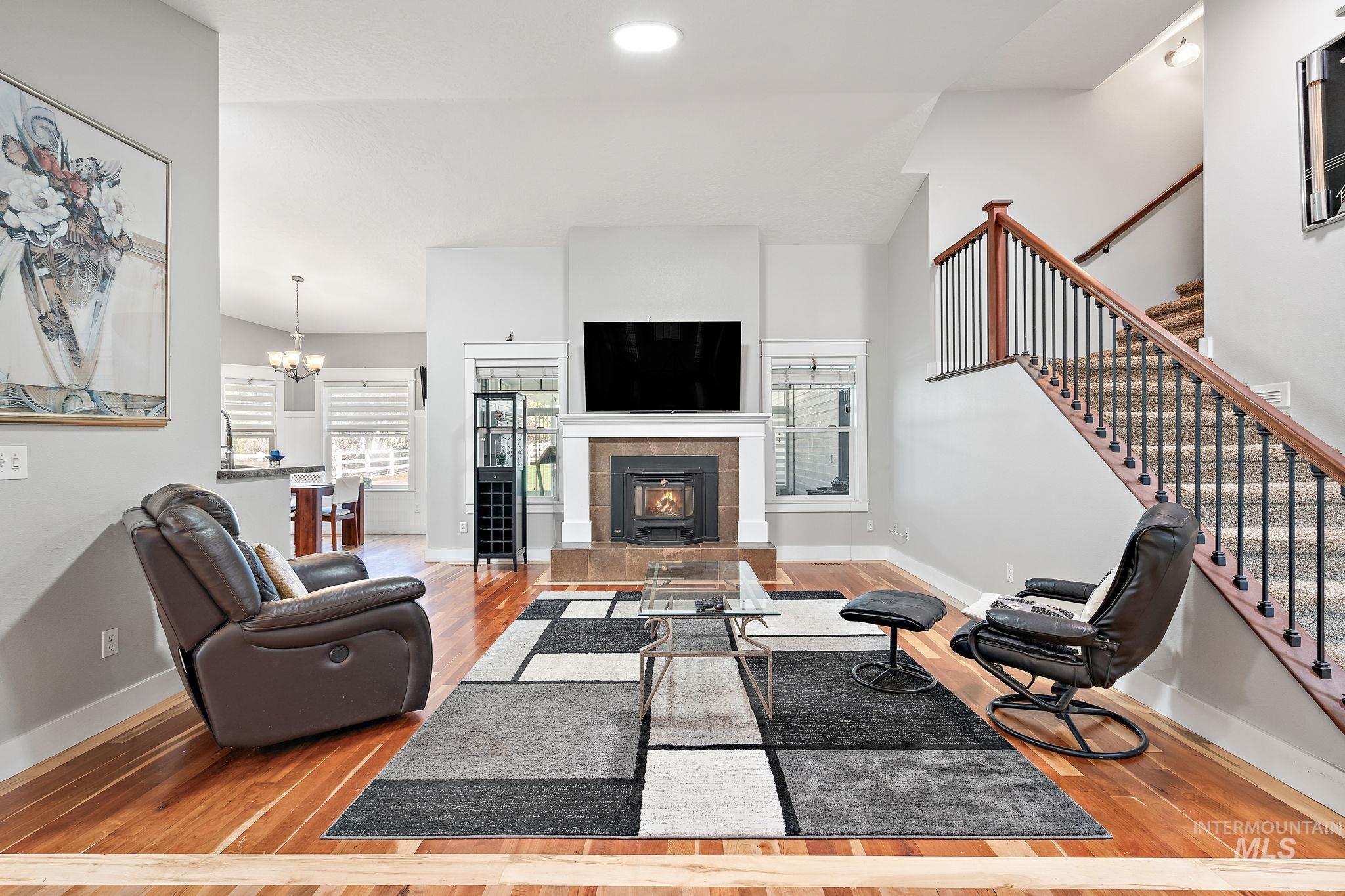 Living area with light wood-type flooring, a tiled fireplace, stairway, a chandelier, and recessed lighting