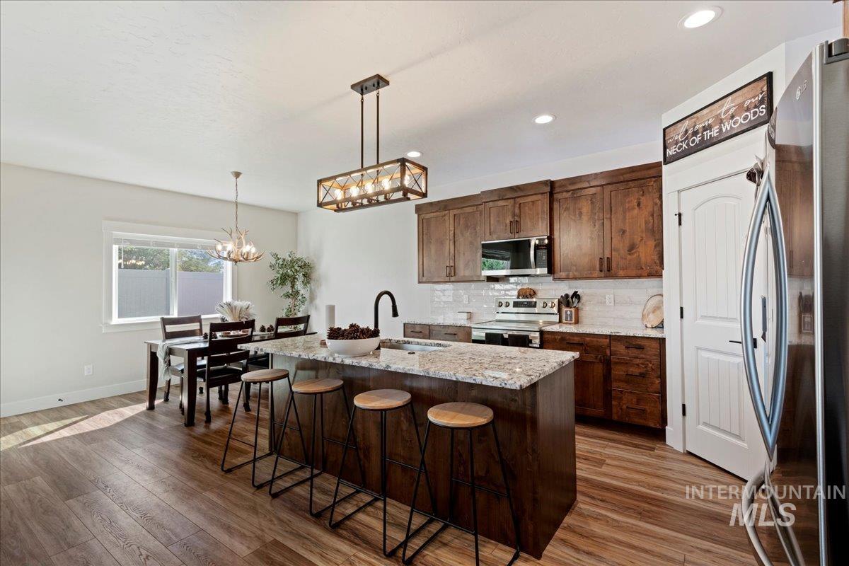 Kitchen with stainless steel appliances, decorative backsplash, light stone countertops, hanging light fixtures, and an island with sink
