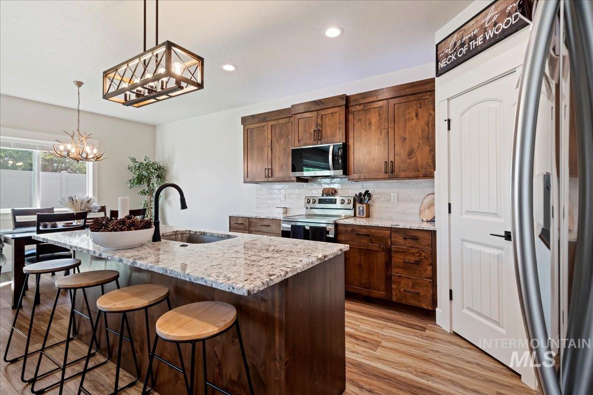 Kitchen featuring hanging light fixtures, stainless steel appliances, decorative backsplash, an island with sink, and light stone counters
