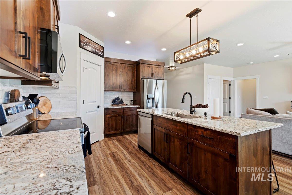 Kitchen with decorative light fixtures, a center island with sink, appliances with stainless steel finishes, open floor plan, and light wood-type flooring