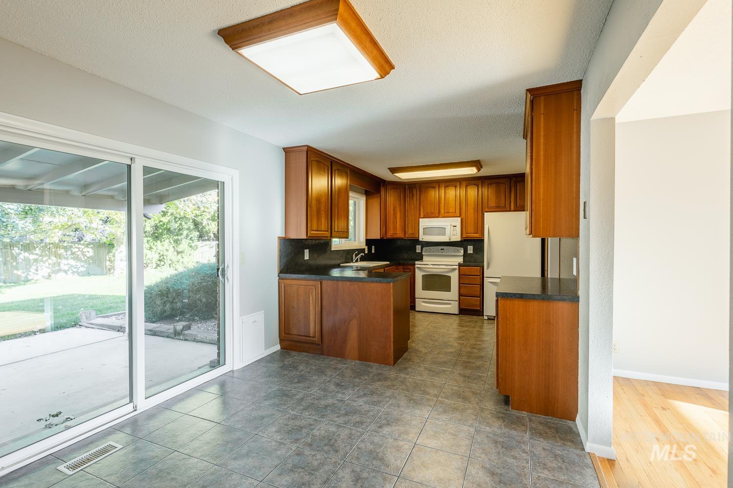 Kitchen with dark countertops, white appliances, tasteful backsplash, brown cabinetry, and a peninsula