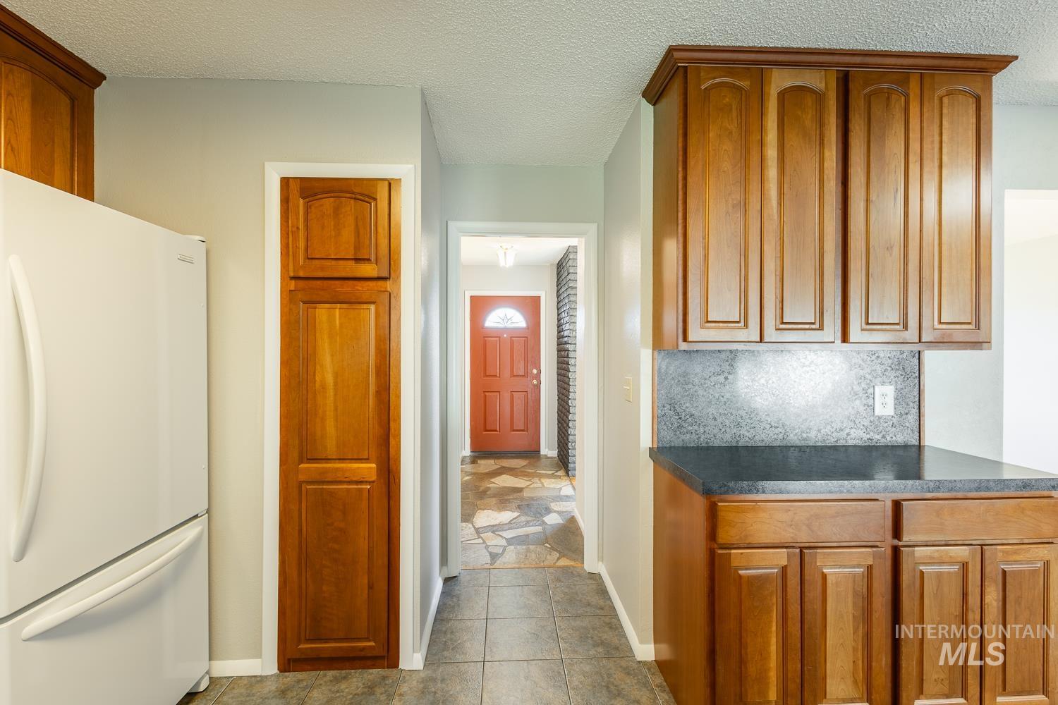 Kitchen featuring freestanding refrigerator, brown cabinets, a textured ceiling, dark tile patterned flooring, and decorative backsplash