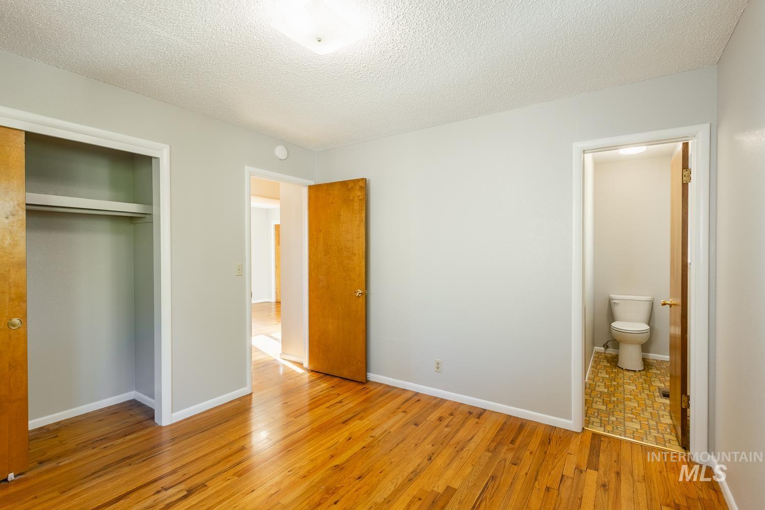 Unfurnished bedroom with light wood finished floors, a textured ceiling, a closet, and ensuite bathroom