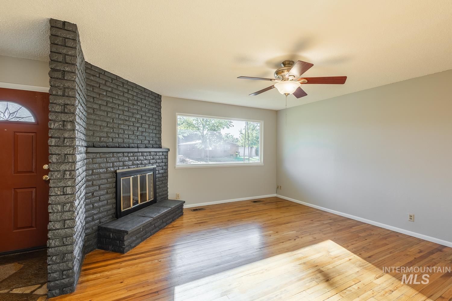 Unfurnished living room featuring light wood-type flooring, a brick fireplace, and ceiling fan