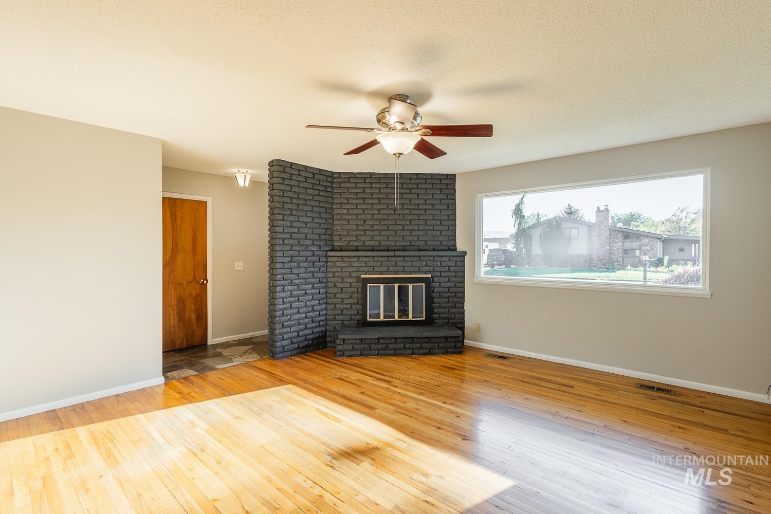 Unfurnished living room with light wood finished floors, a ceiling fan, and a brick fireplace