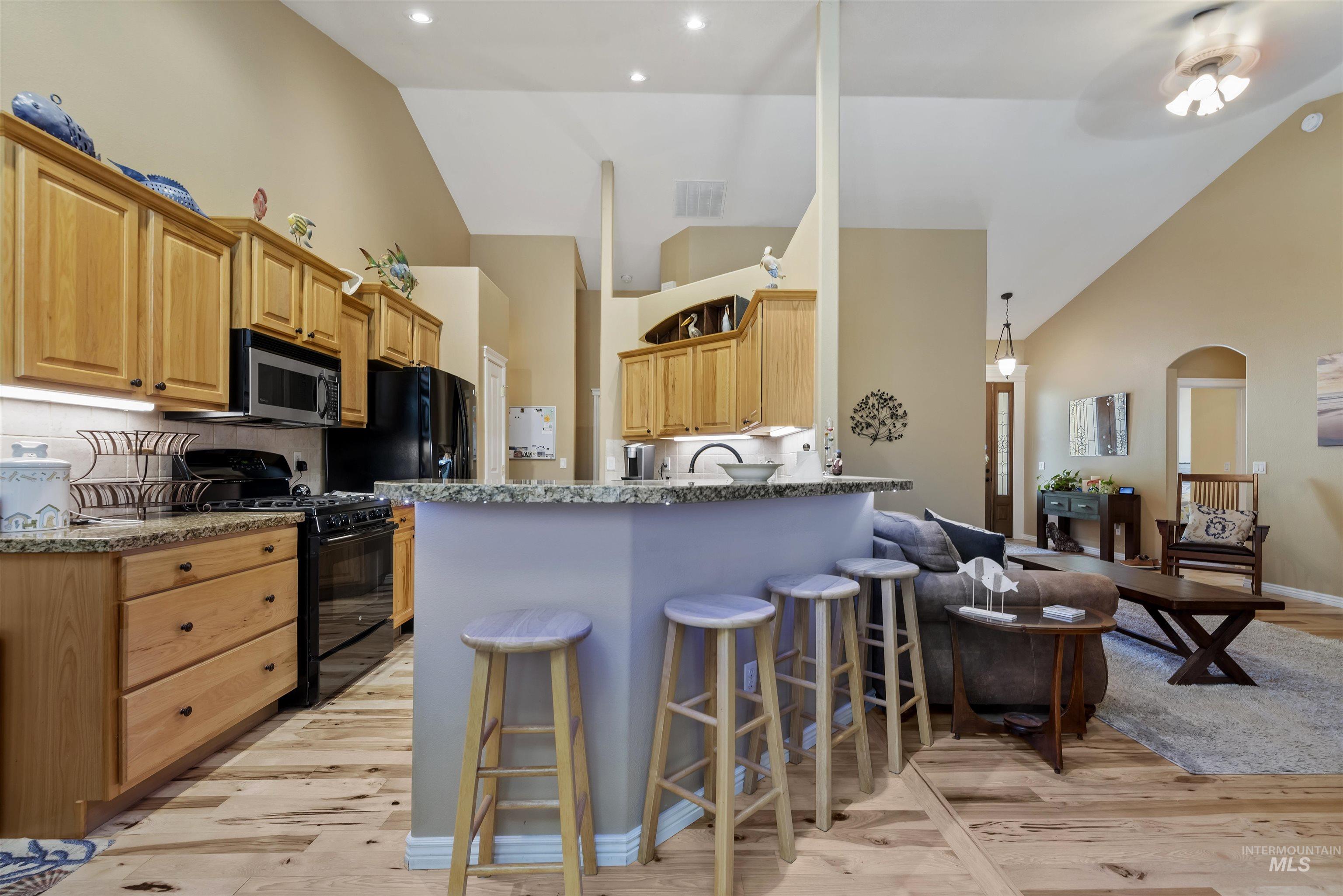 Kitchen with black gas range, high vaulted ceiling, light wood-type flooring, a peninsula, and a kitchen breakfast bar