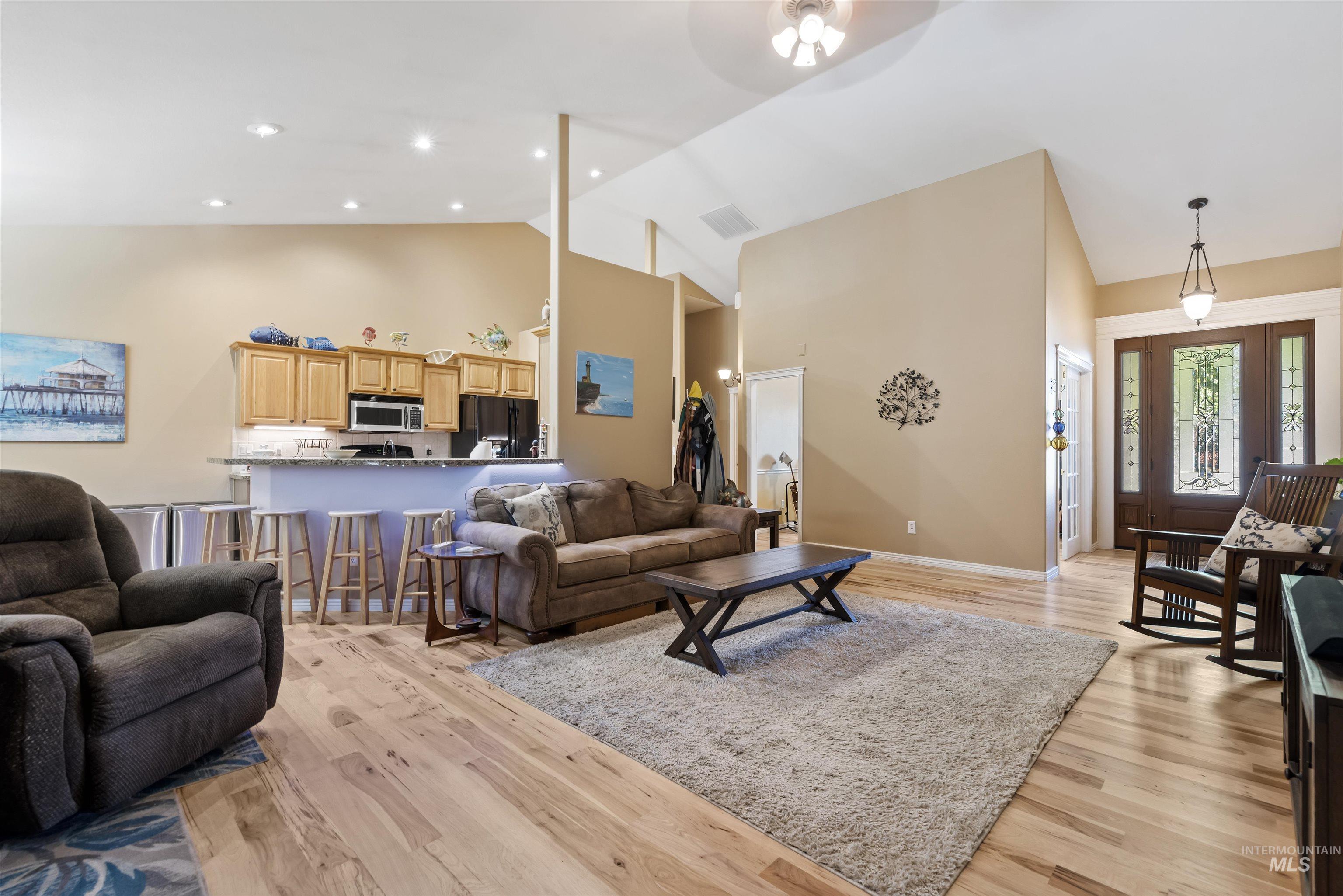Living area with light wood-style flooring, high vaulted ceiling, and recessed lighting