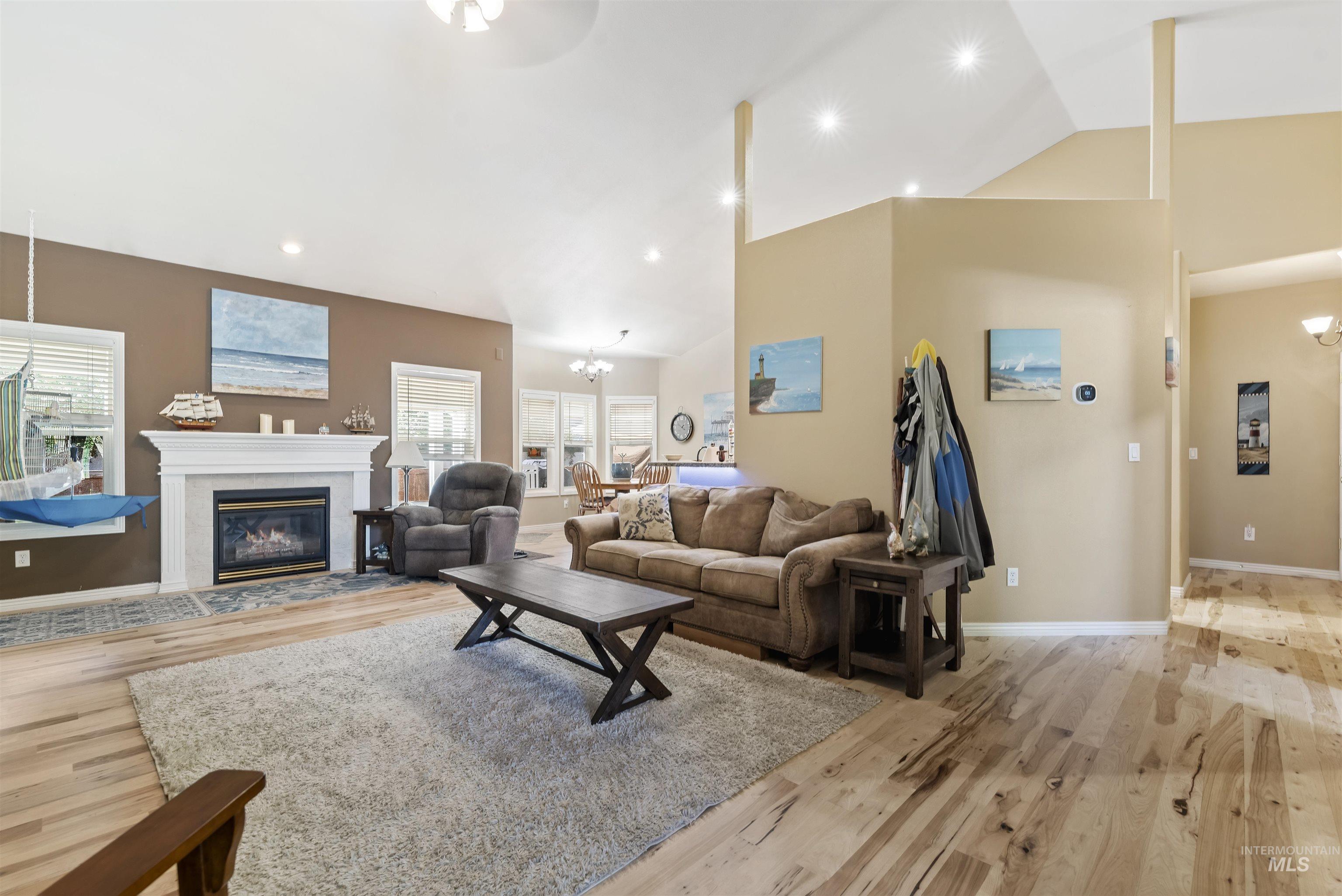 Living room featuring a chandelier, high vaulted ceiling, a fireplace, light wood-type flooring, and recessed lighting