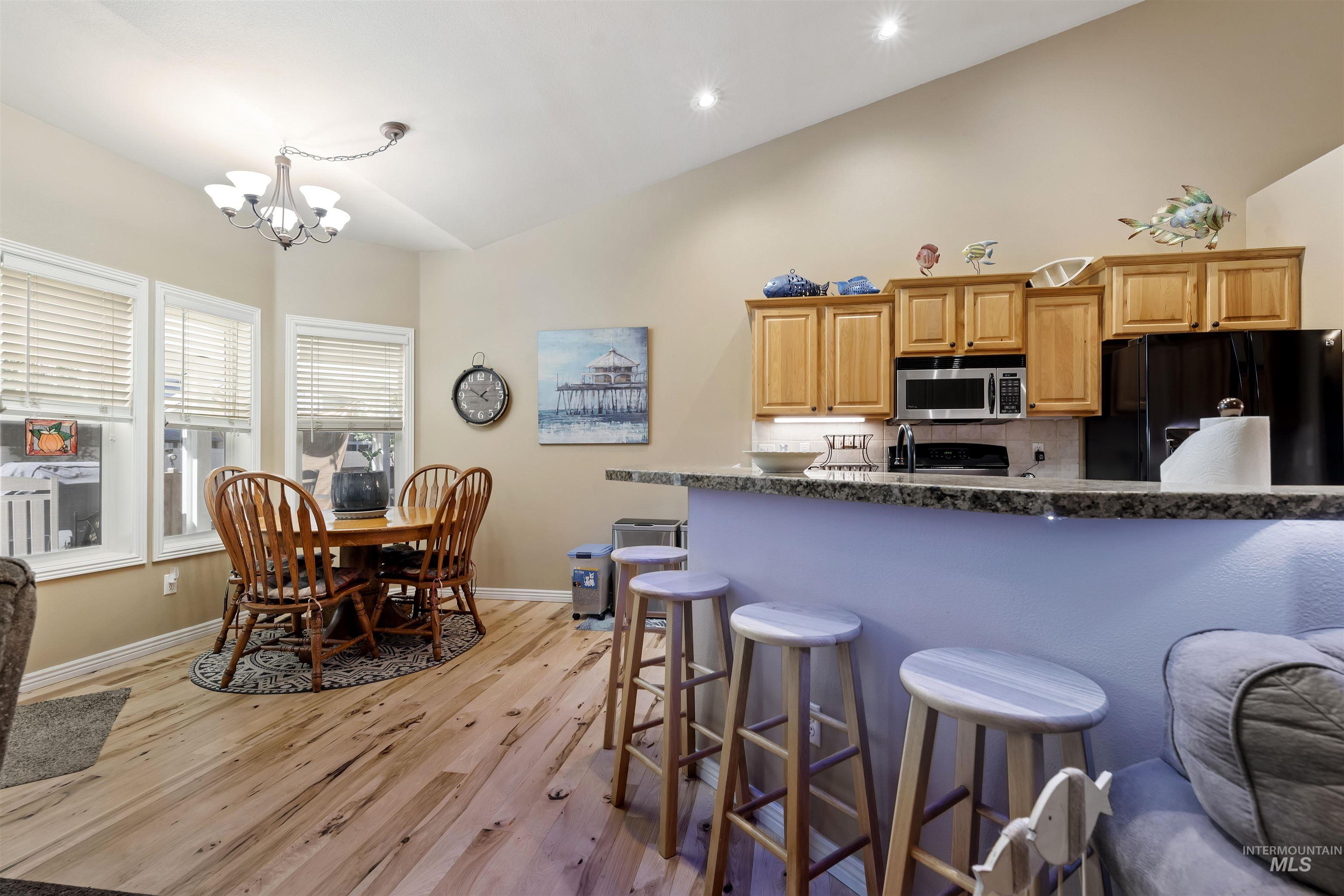 Kitchen featuring black refrigerator with ice dispenser, a breakfast bar area, light wood-style floors, stainless steel microwave, and high vaulted ceiling