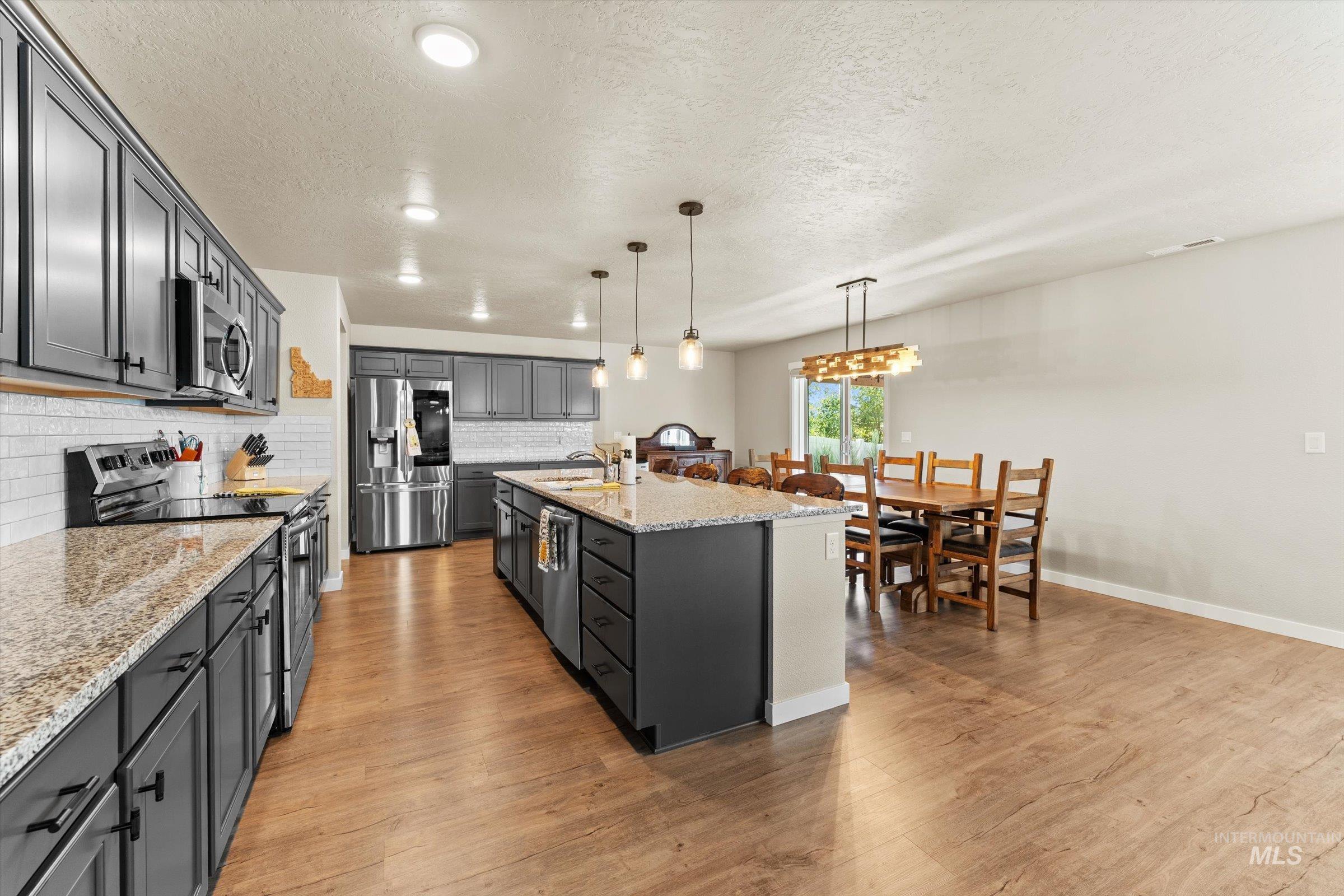 Kitchen featuring stainless steel appliances, light stone counters, decorative light fixtures, light wood-style flooring, and tasteful backsplash