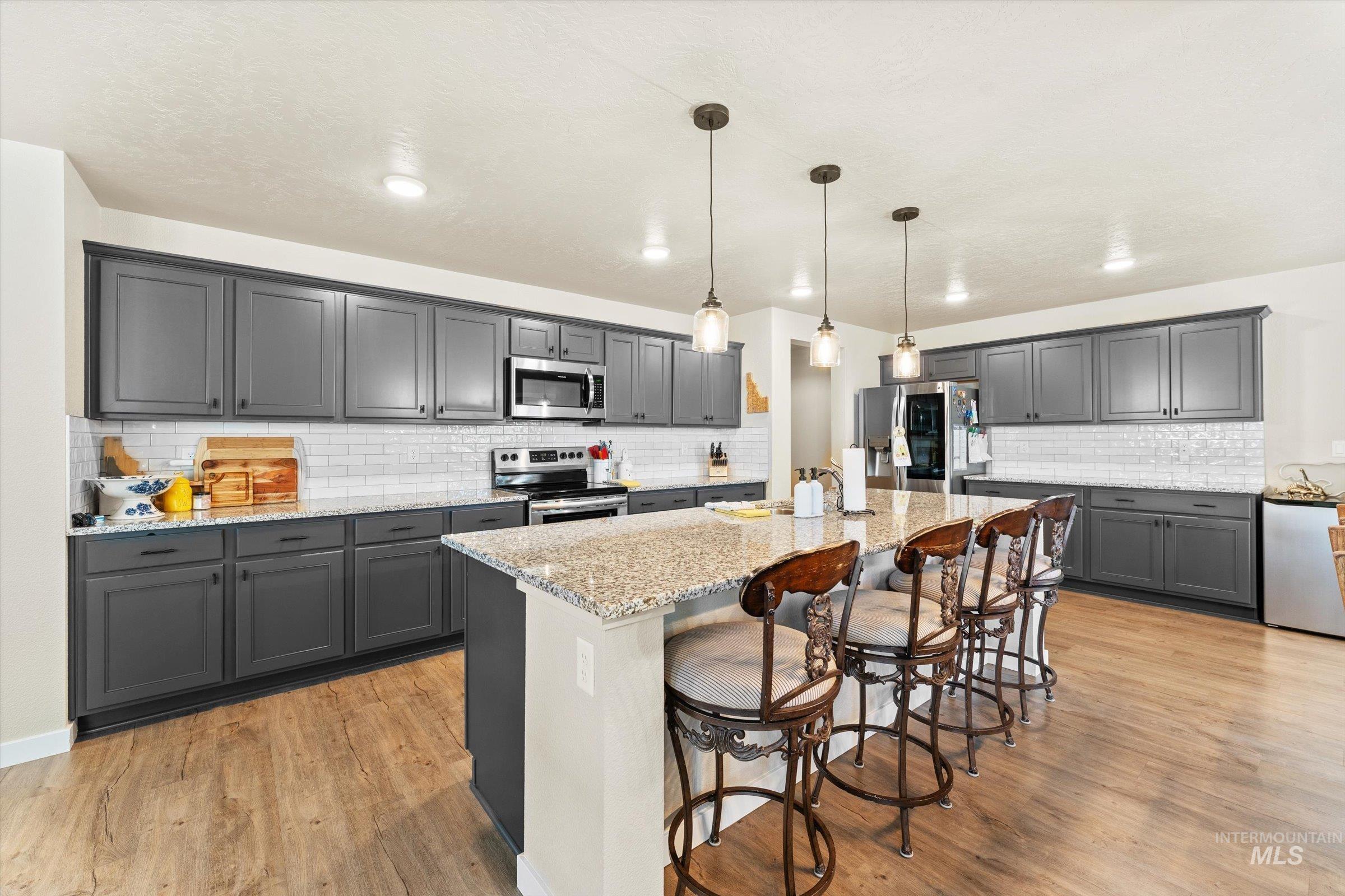 Kitchen with light stone counters, decorative light fixtures, a kitchen breakfast bar, and backsplash