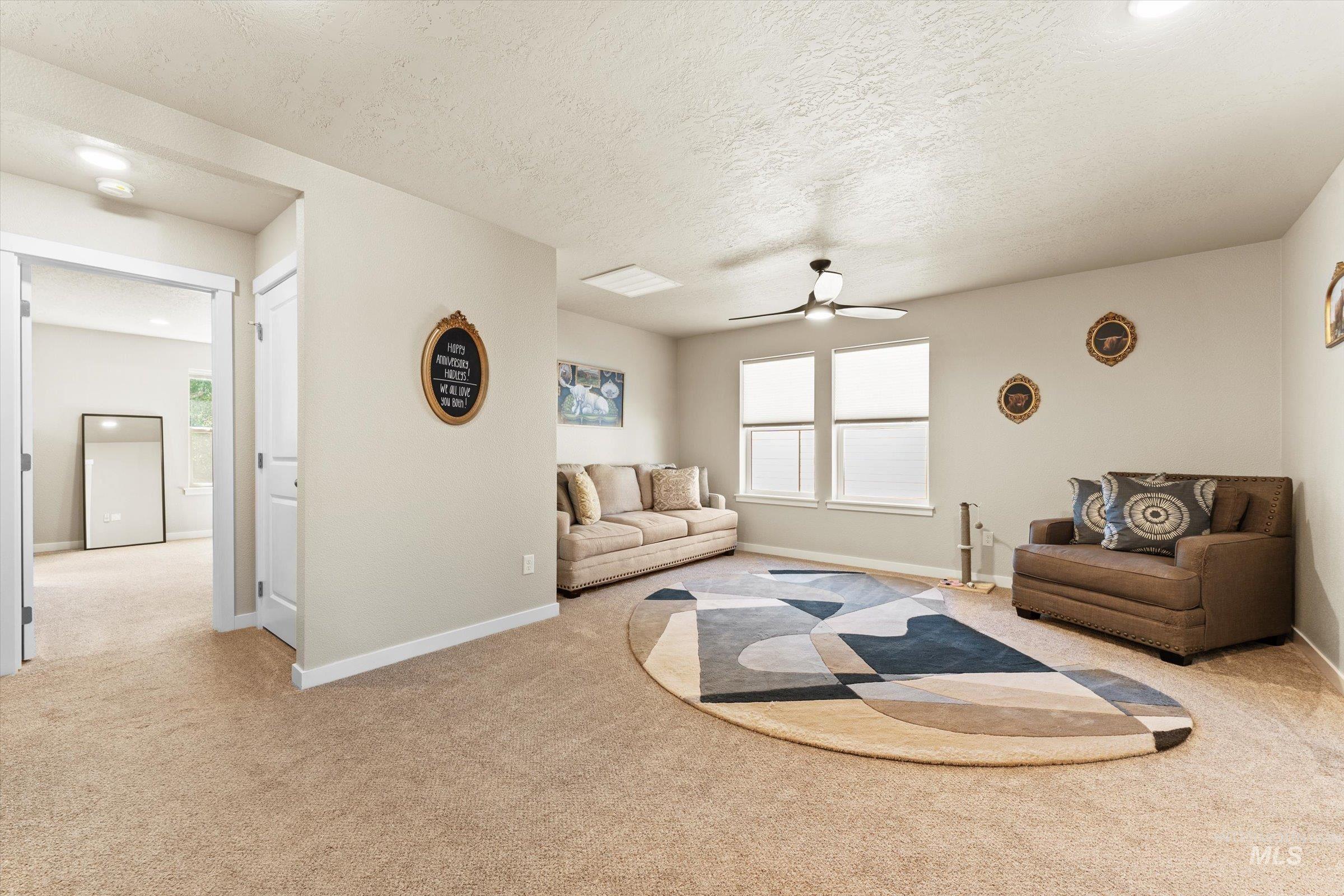 Living area featuring a ceiling fan, light carpet, and a textured ceiling