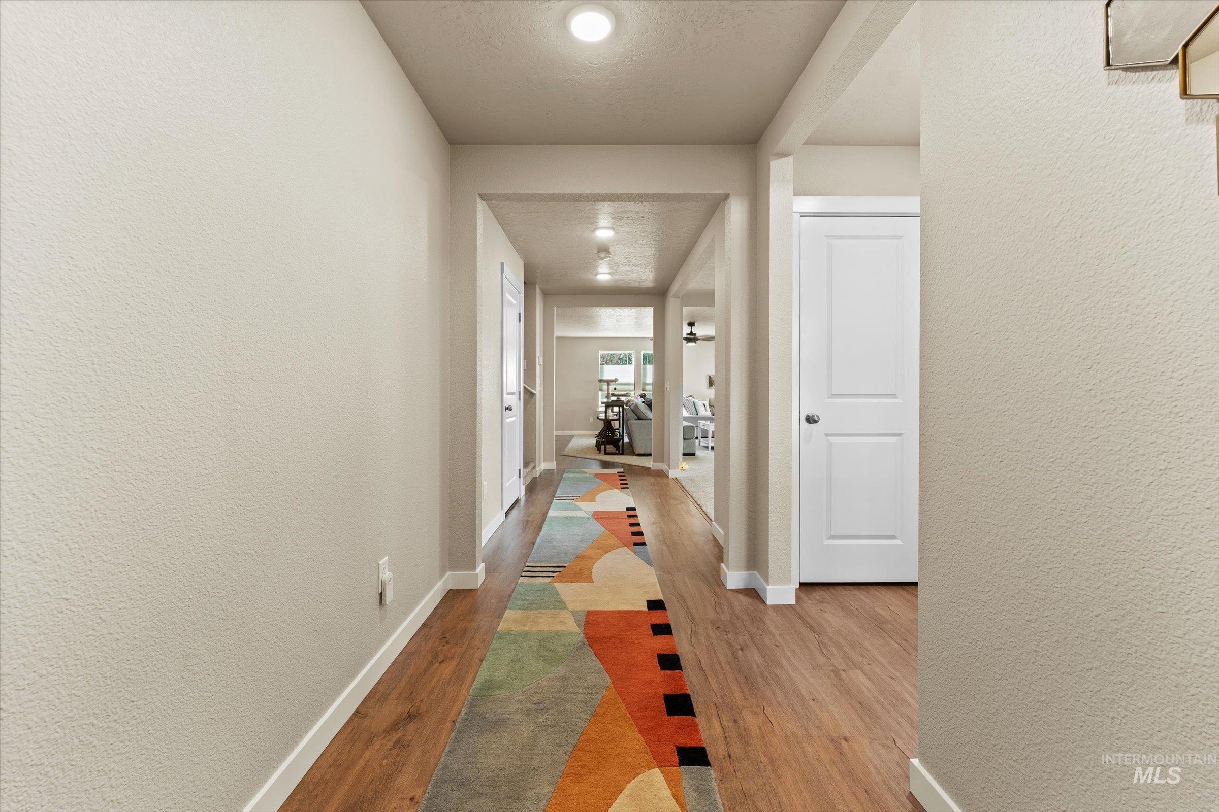 Hall with a textured wall, light wood finished floors, and a textured ceiling