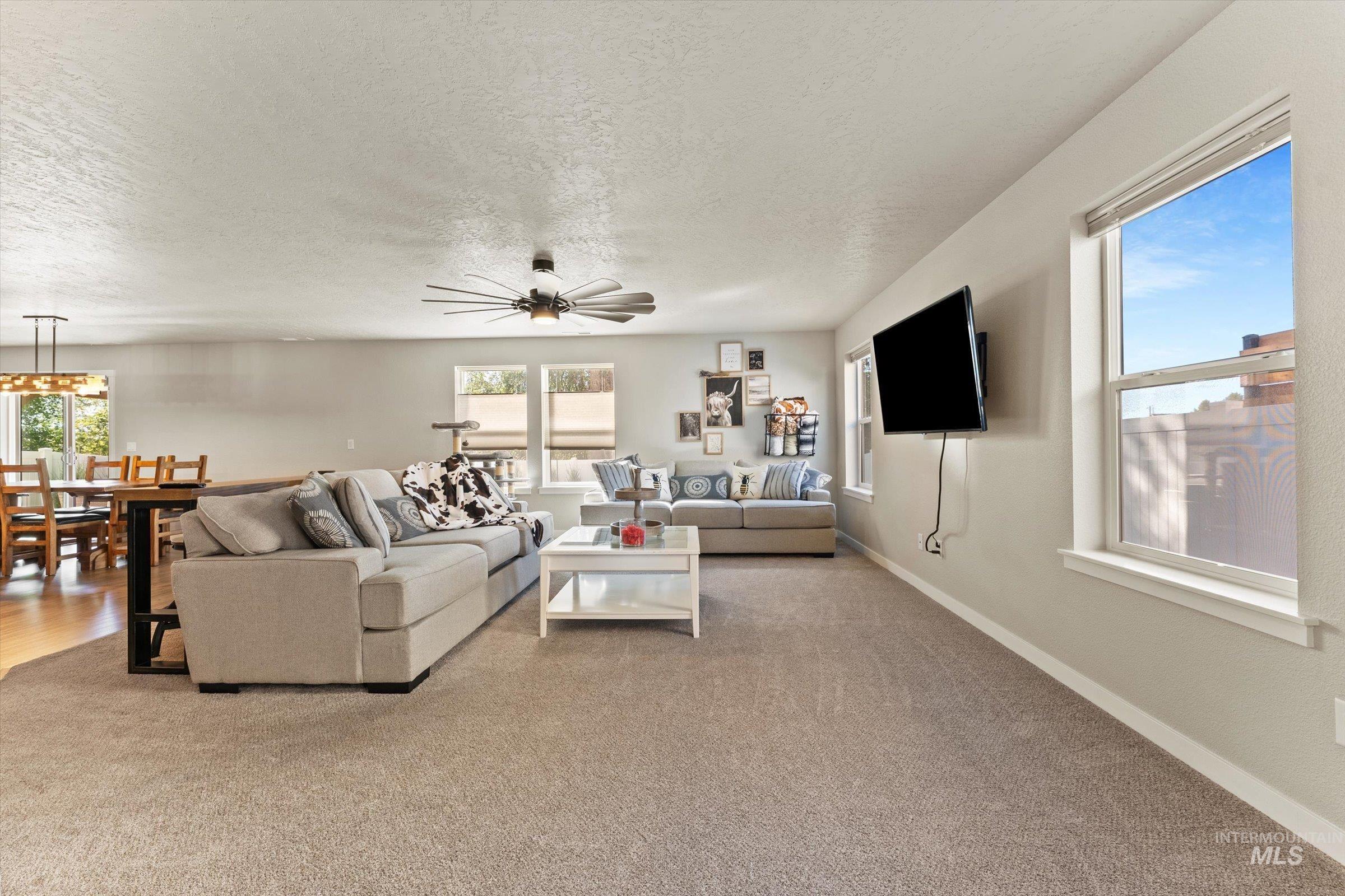 Living room with a textured ceiling, carpet floors, and ceiling fan