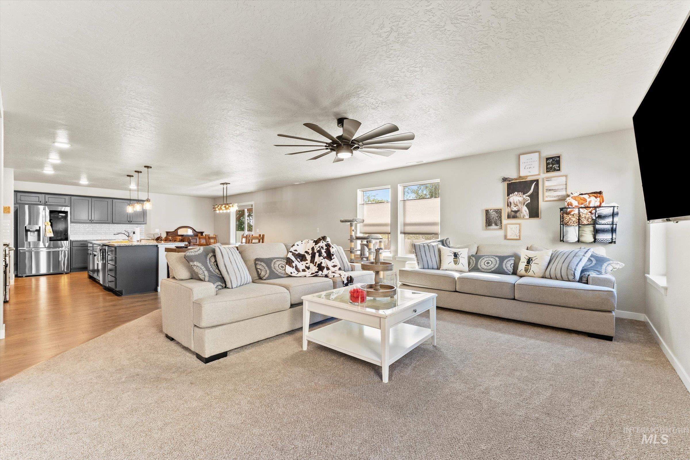 Living area featuring a textured ceiling, ceiling fan, a chandelier, and light colored carpet