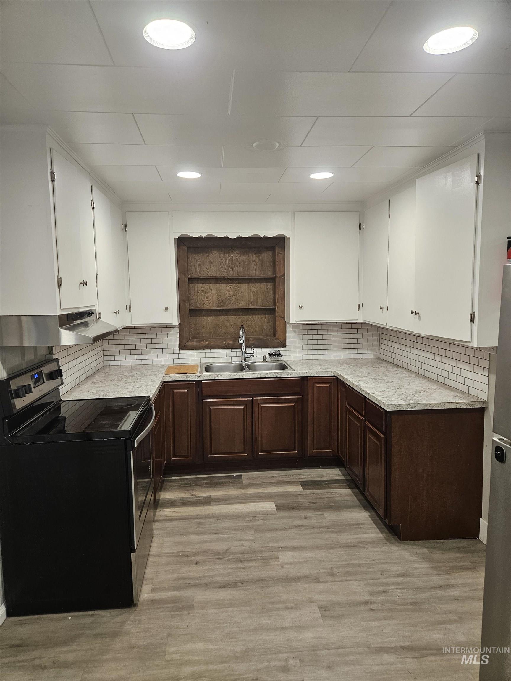 Kitchen with stainless steel range with electric stovetop, dark brown cabinetry, backsplash, white cabinets, and light wood-style floors