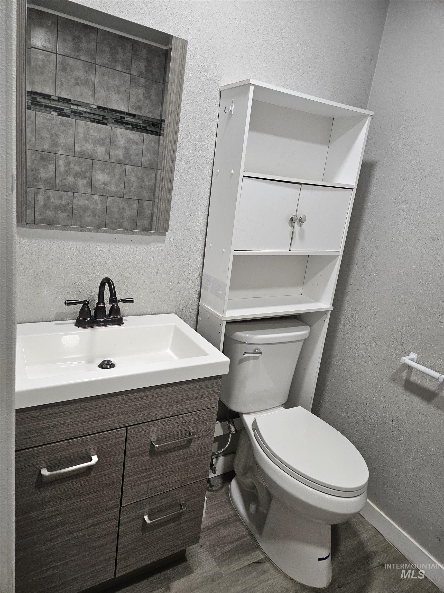 Bathroom with a textured wall, vanity, and dark wood-type flooring