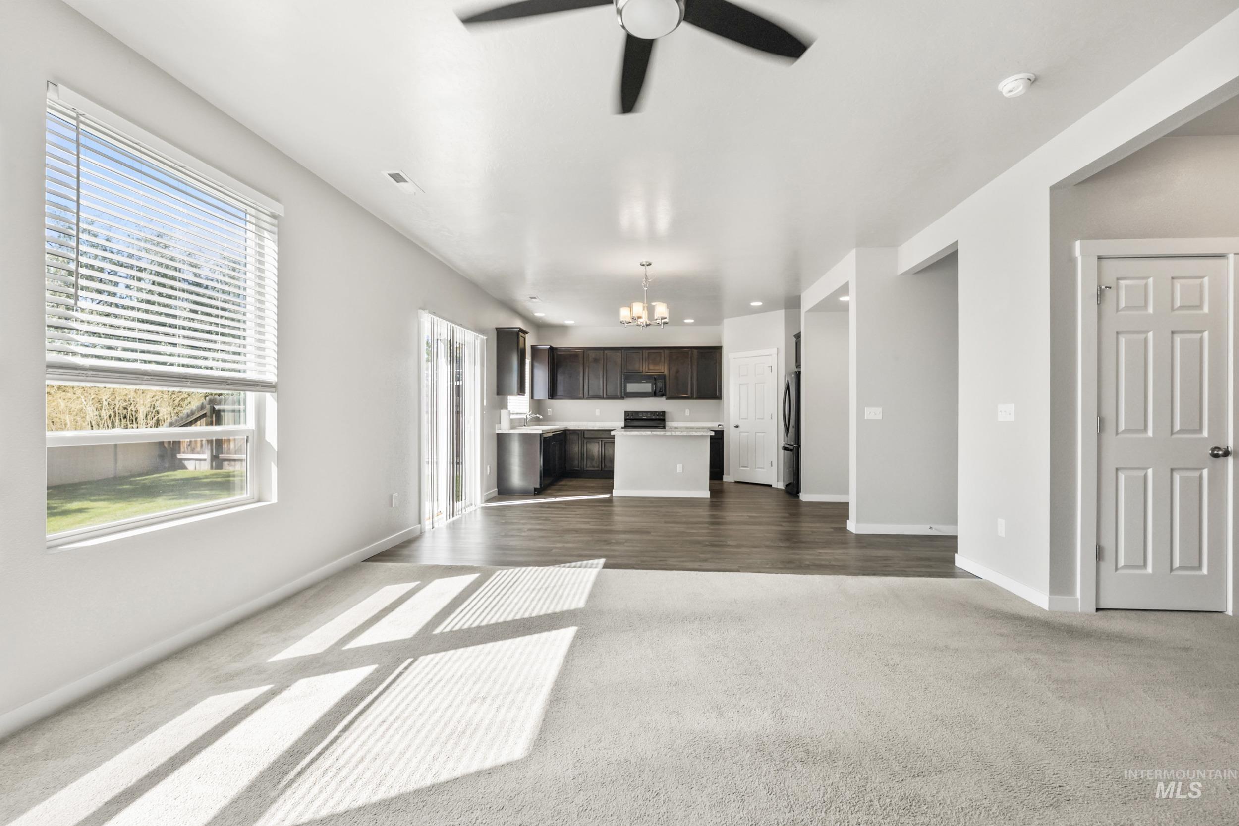 Unfurnished living room with dark carpet, a chandelier, and ceiling fan