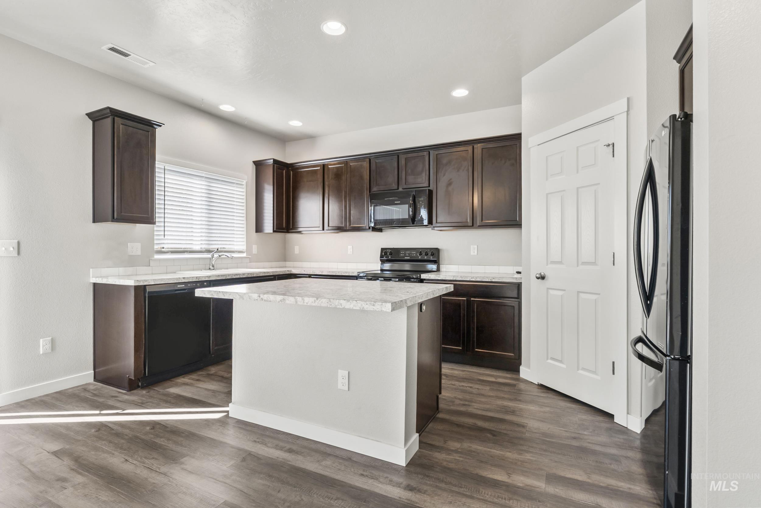 Kitchen with light countertops, black appliances, dark brown cabinetry, dark wood-style flooring, and recessed lighting