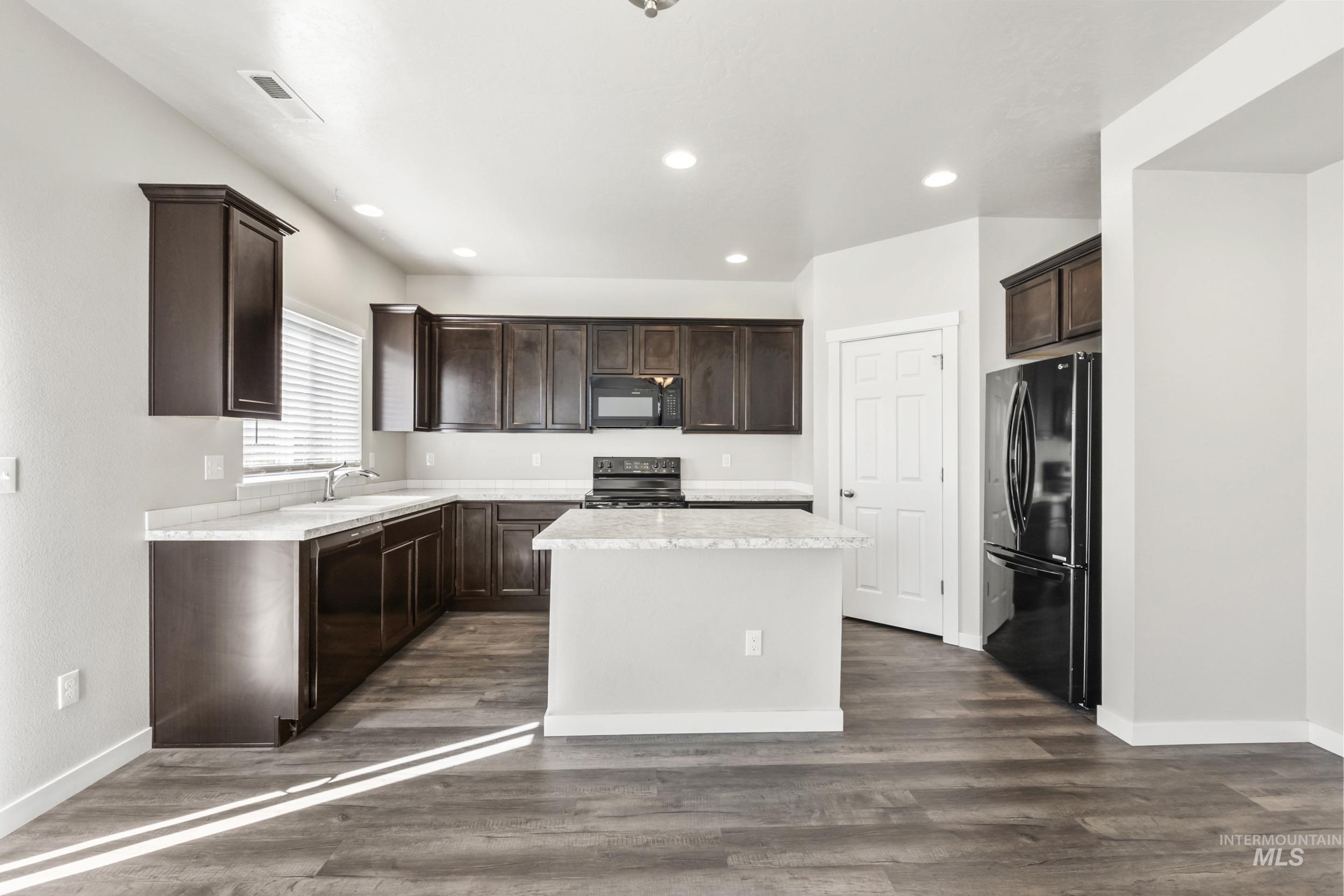 Kitchen with light countertops, dark brown cabinets, black appliances, dark wood-type flooring, and recessed lighting