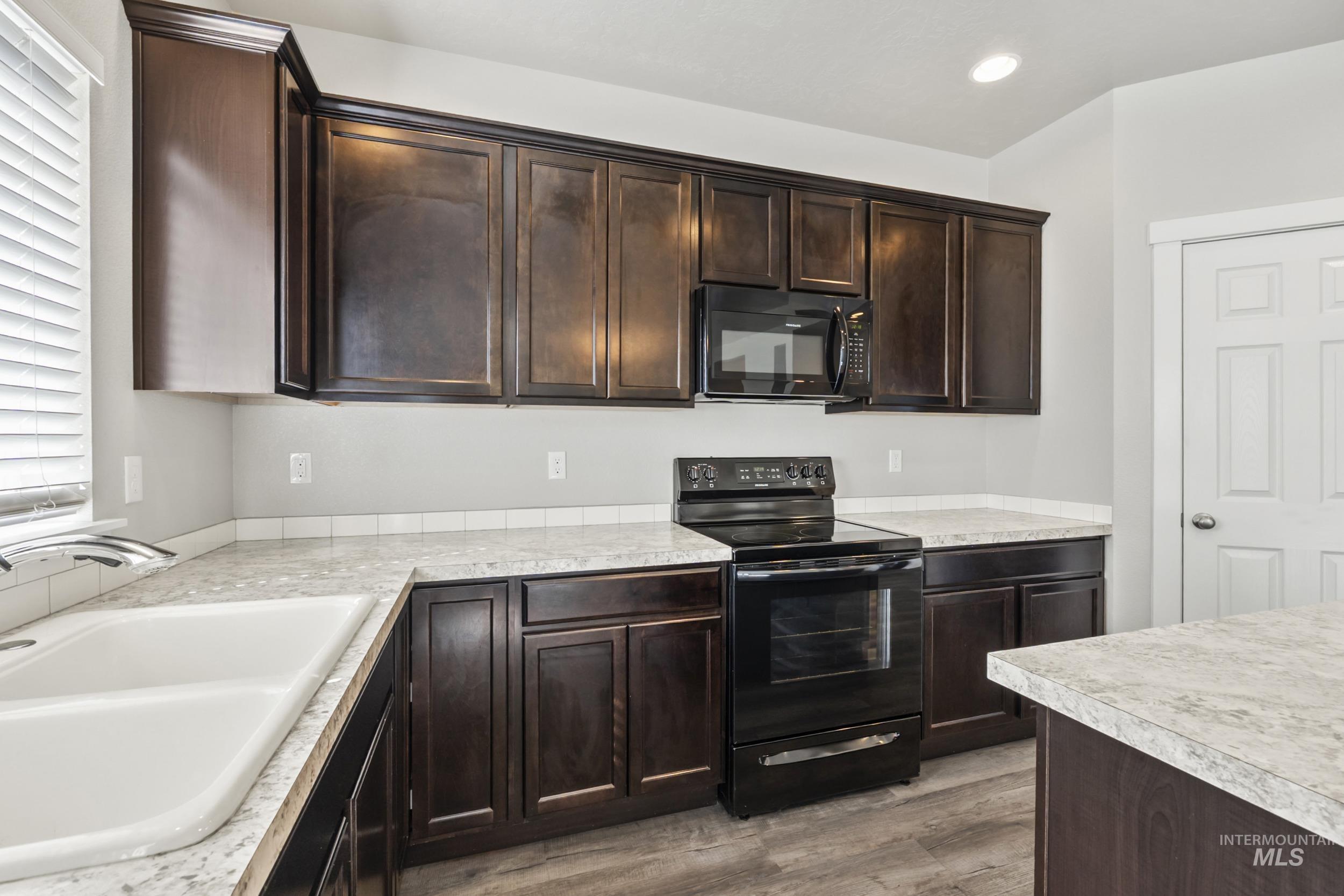 Kitchen featuring black appliances, dark brown cabinets, light countertops, and recessed lighting